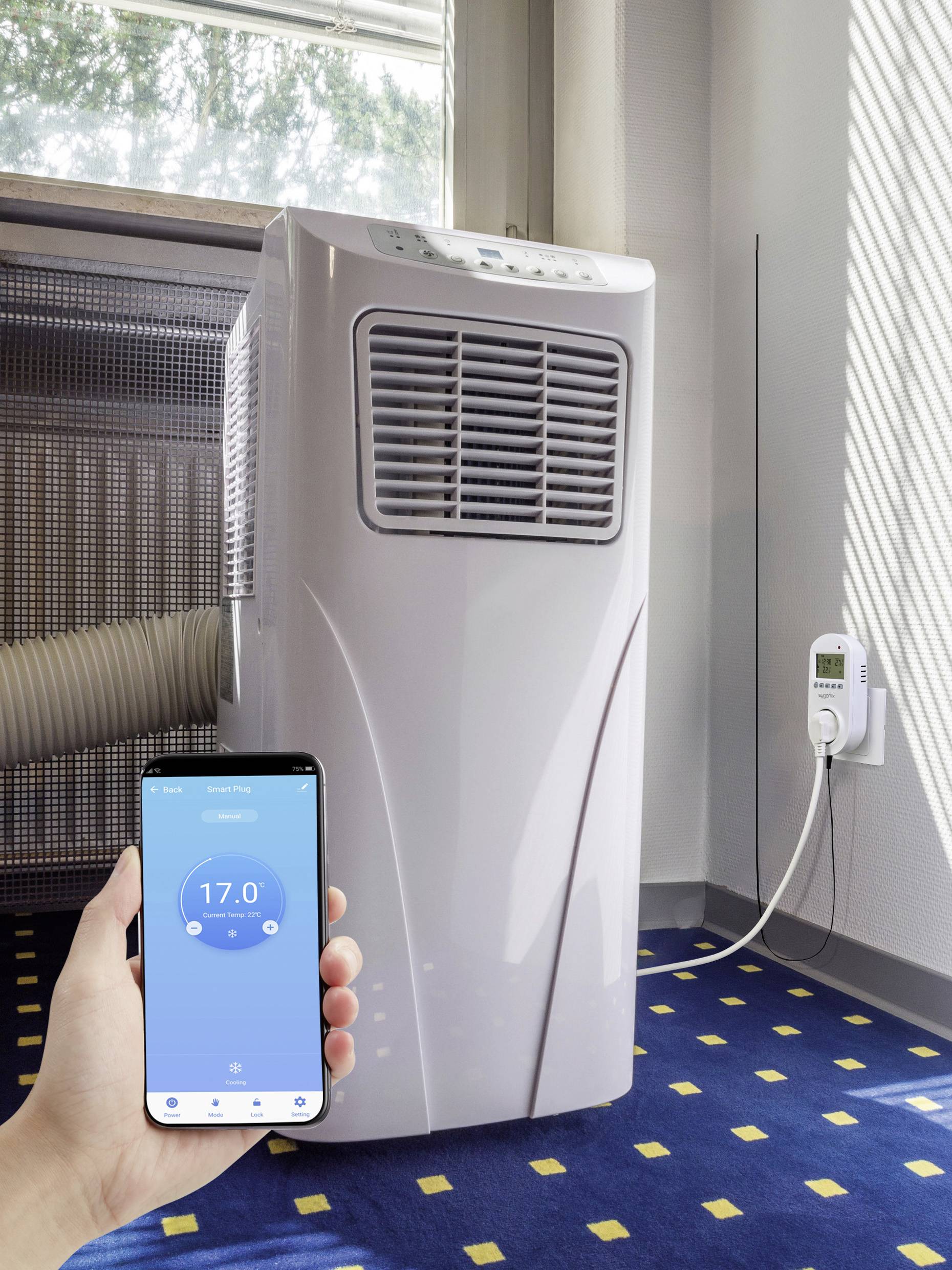 A hand holds a smartphone with an app displaying 17 degrees. In the background stands a switched-on portable air conditioning unit.
