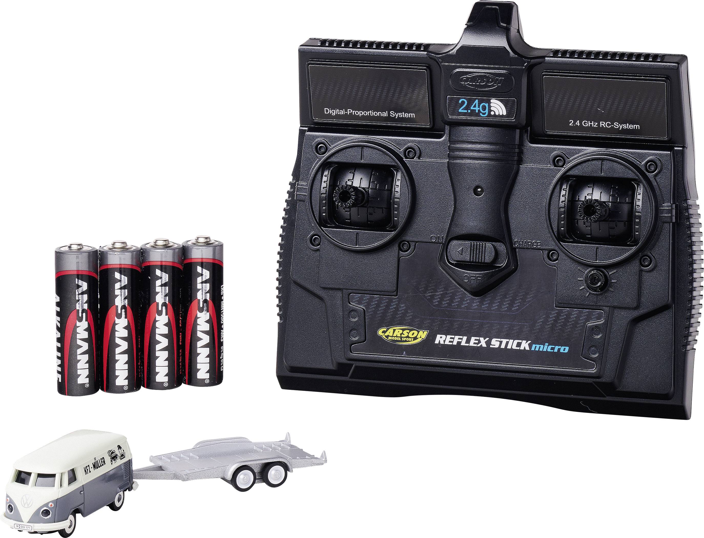 A black 2.4 GHz RC remote control with two control sticks, alongside four AA batteries and a small model car with a trailer.