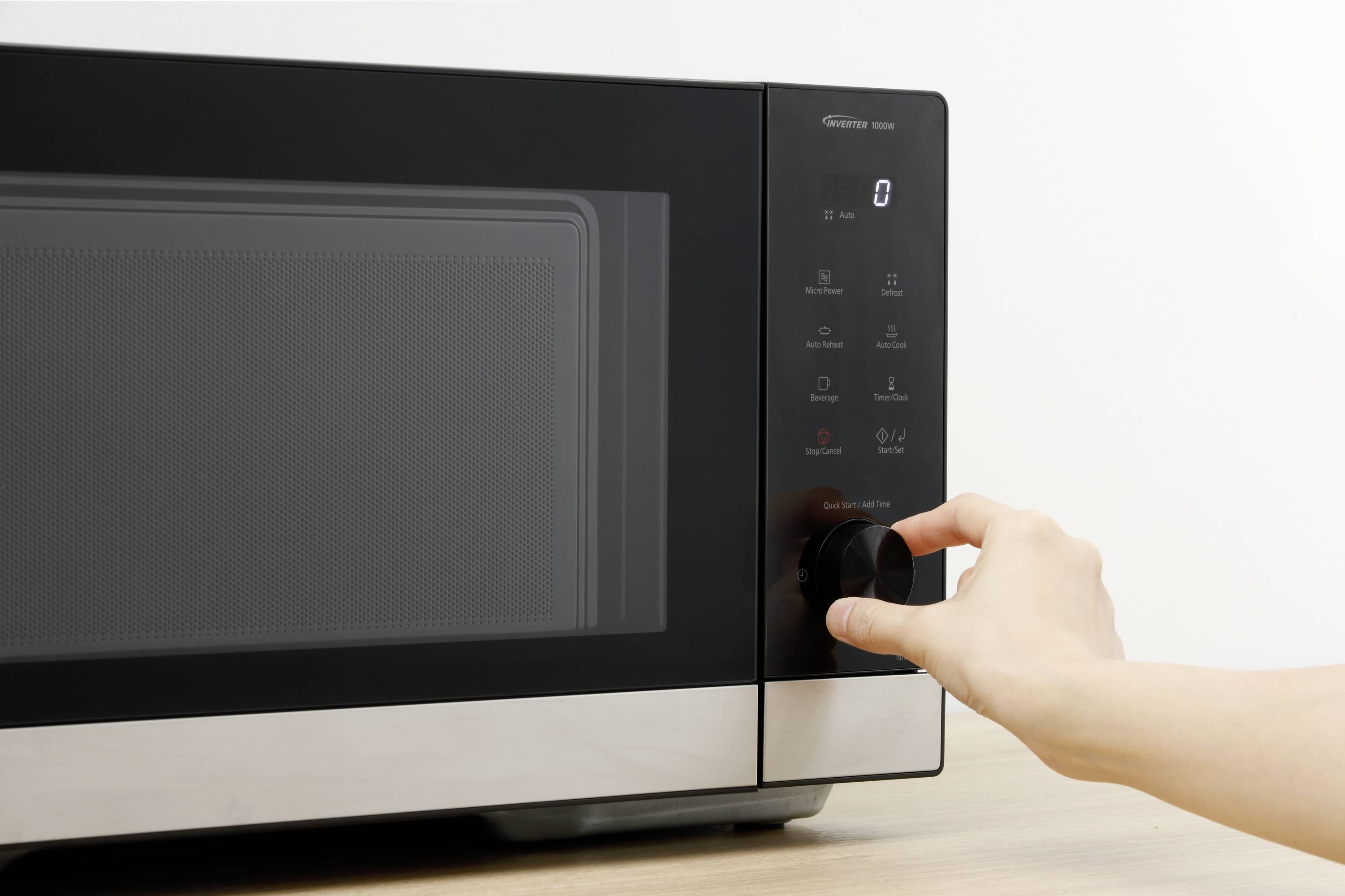 A hand turns the dial on a black microwave placed on a wooden table.
