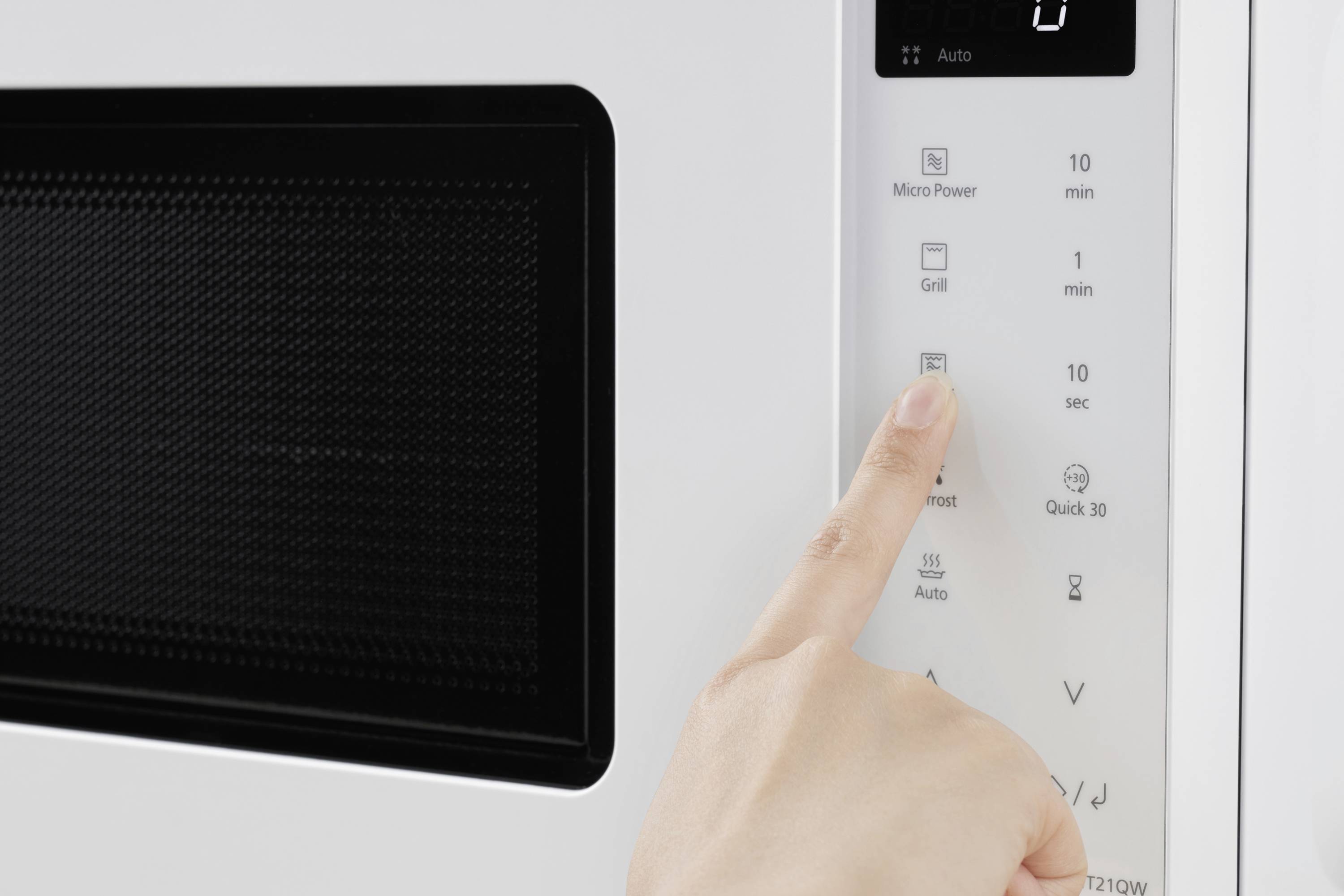 A hand presses the start button on a microwave. The control panel displays options such as 'Grill' and 'Micro Power' for different cooking modes.