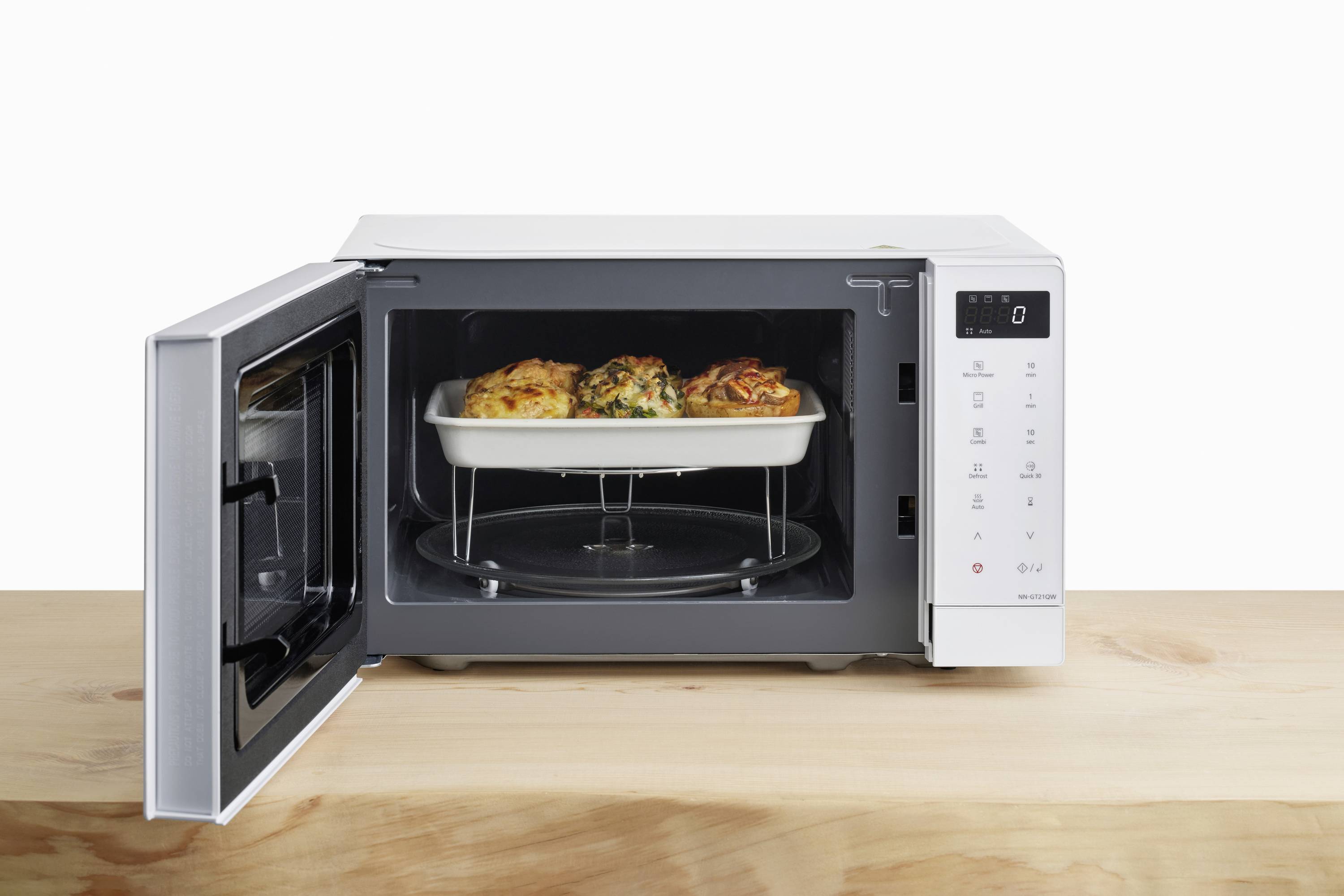 A microwave on a wooden table, heating a dish in a white casserole dish with its door open.