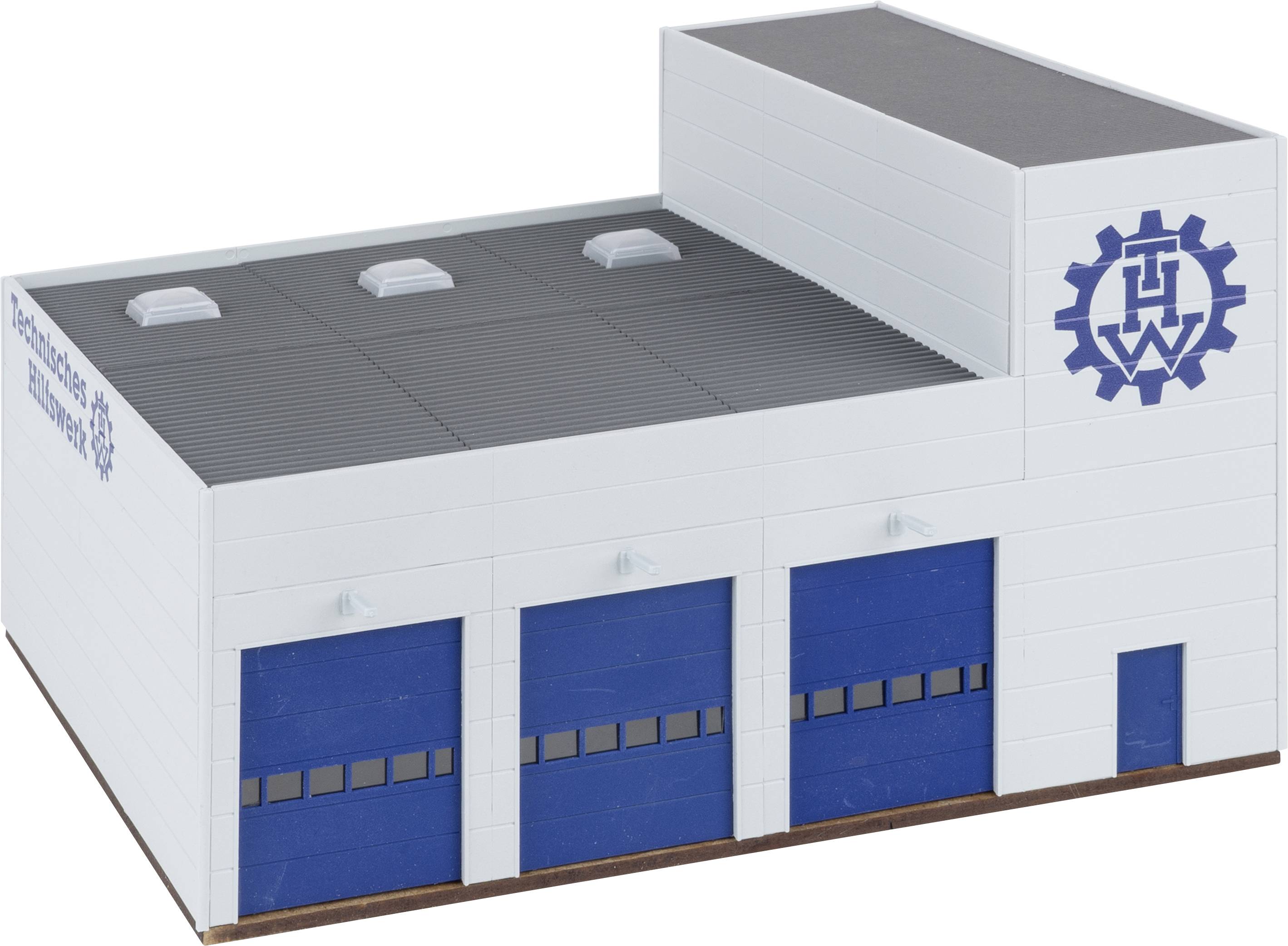 White factory building with three blue doors and a cogwheel logo on the side wall. Flat roof with three roof lights.