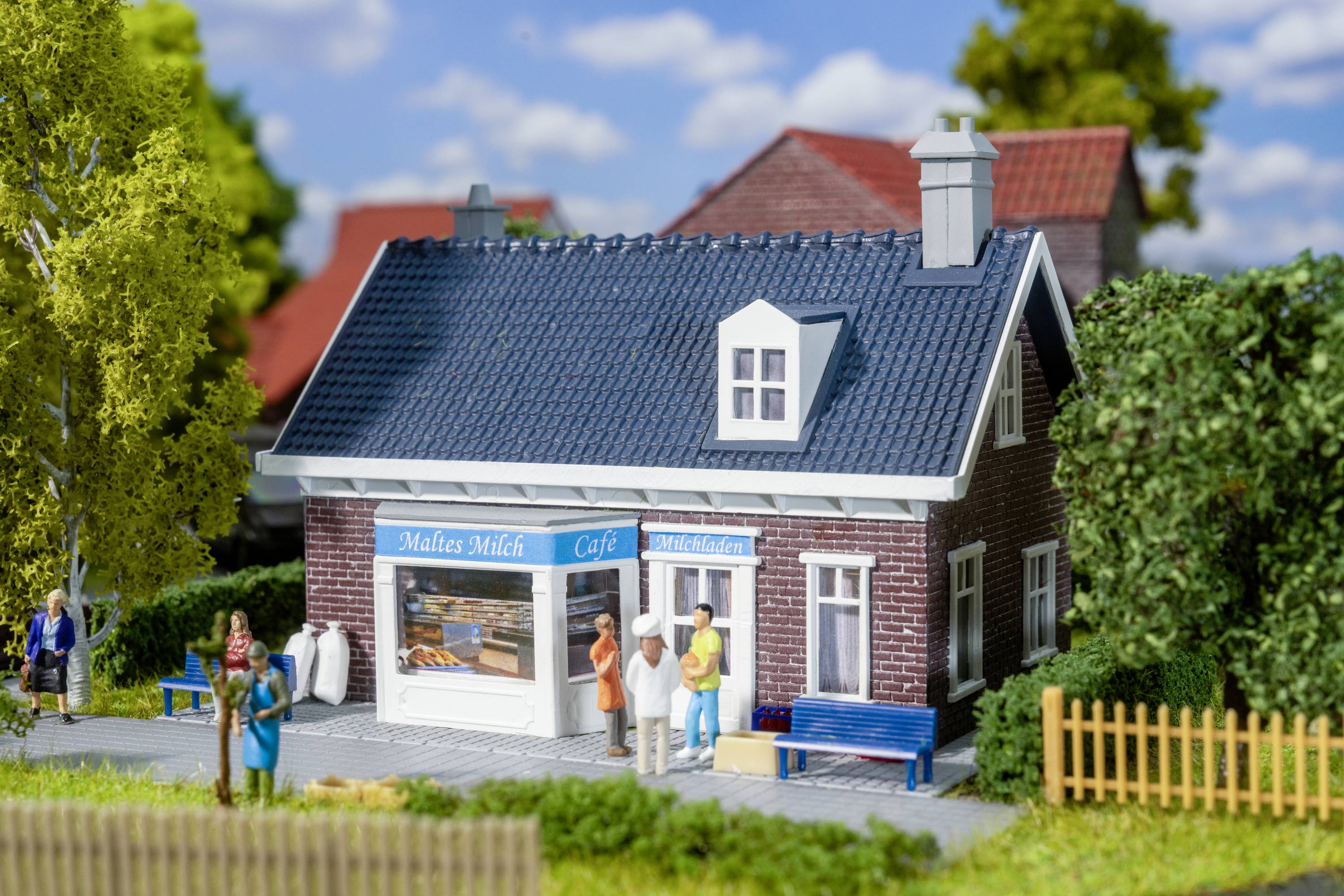 A small model café with the inscription 'Malte's Milk Café', surrounded by miniature trees and figures standing outside.