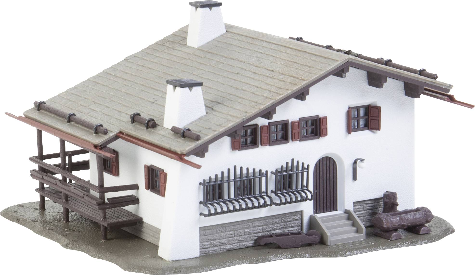 A miniature house in an alpine style with wooden details, red shutters and a small balcony, stands on a grey base.