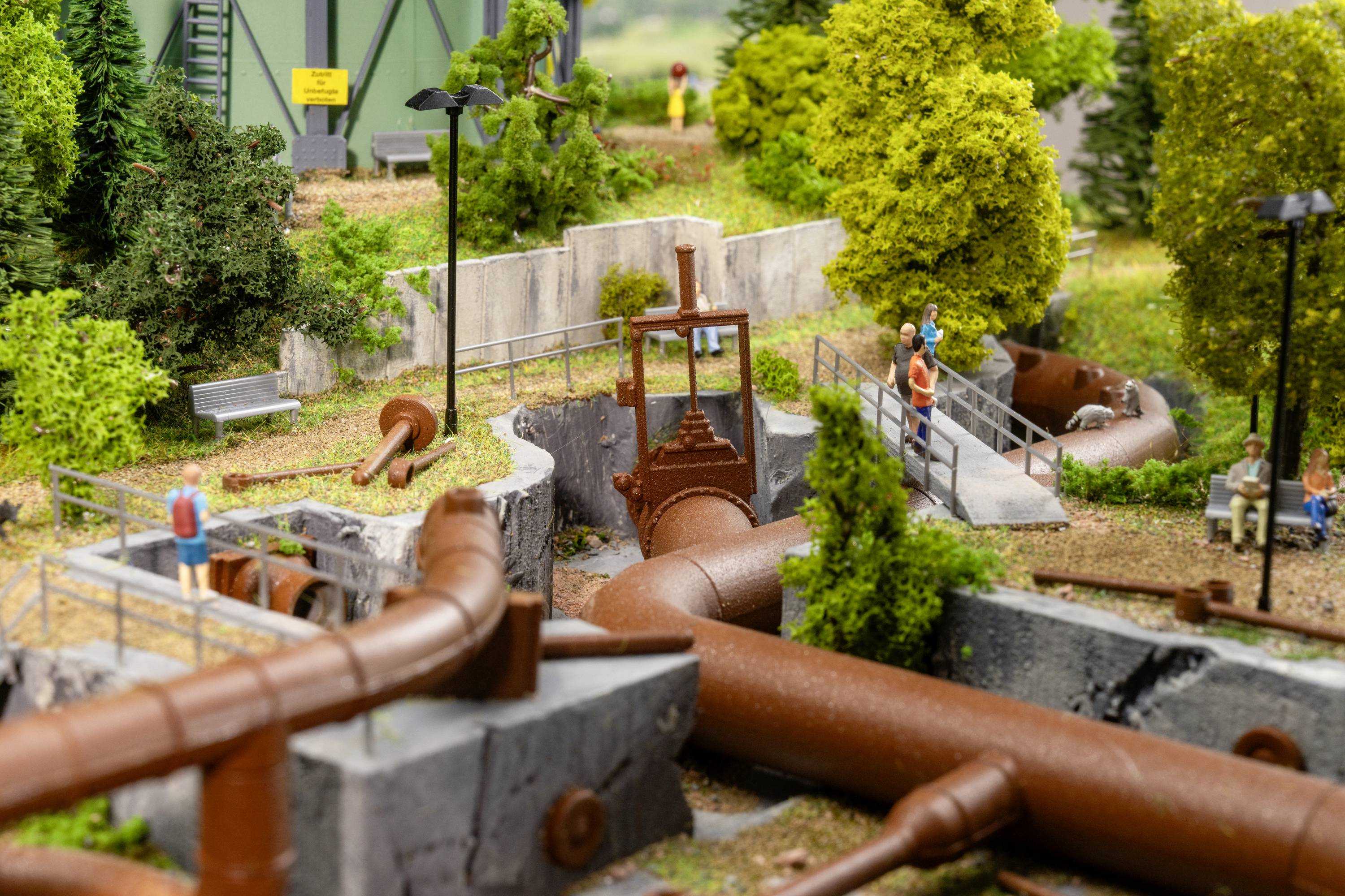 A miniature model landscape depicts an industrial wastewater pipe system, surrounded by trees, figures and small buildings.