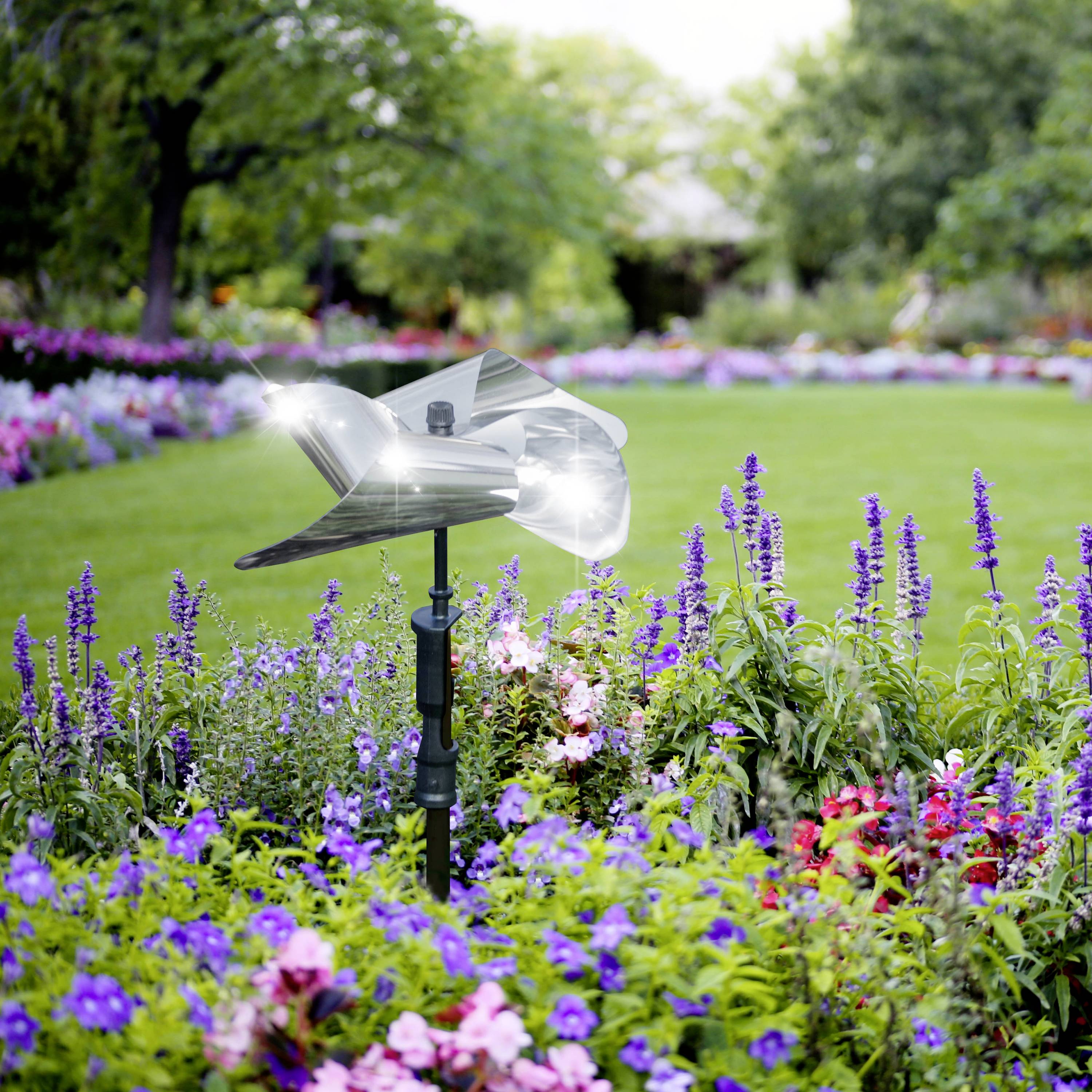 An automated sprinkler system waters a garden with colourful flowers, including large green lawns and various plant species.