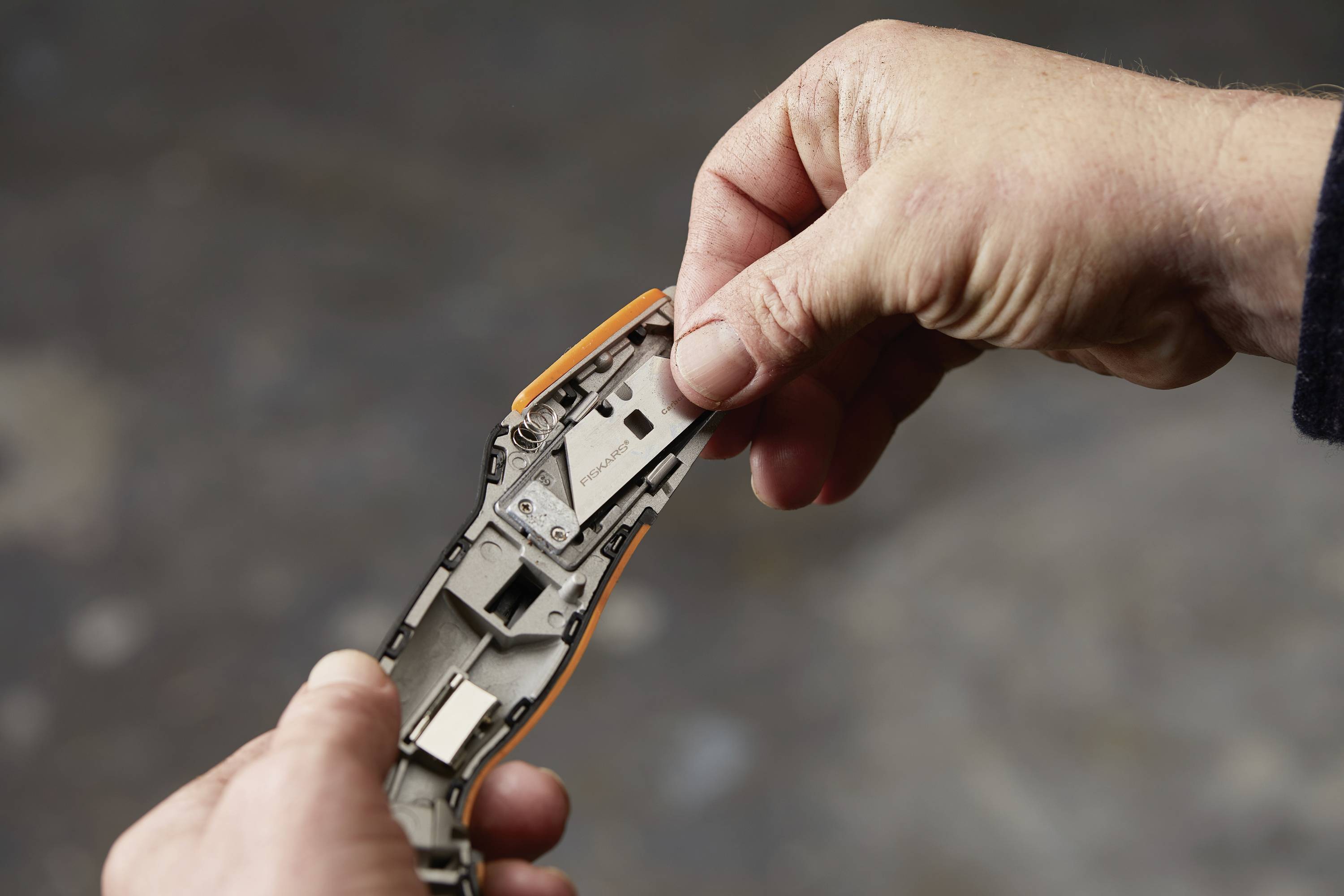Hands are holding an opened, orange-grey wristwatch. One of the hands is carefully removing the battery.