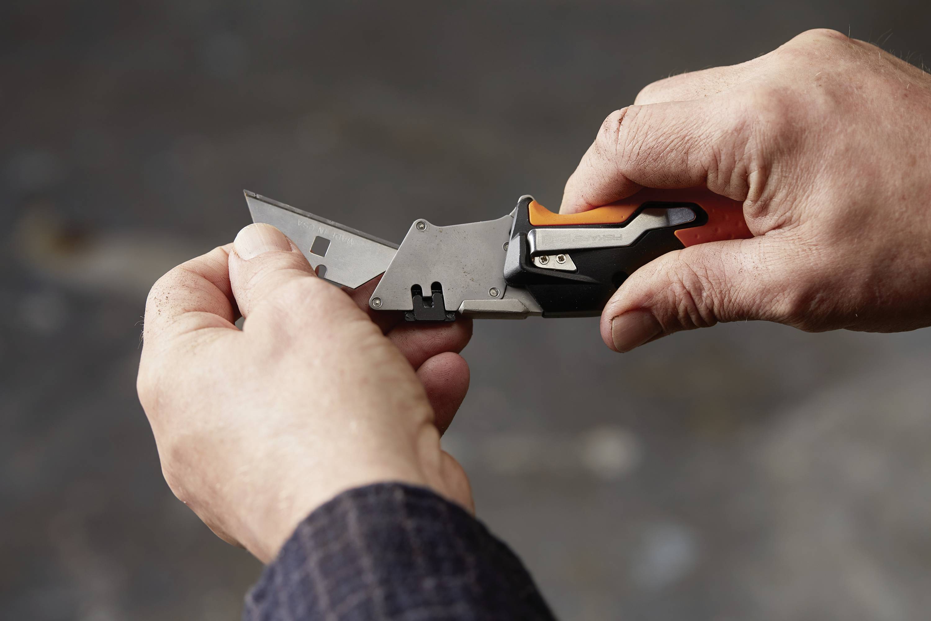 A person is holding a utility knife in both hands and carefully extending the blade. The background is out of focus.