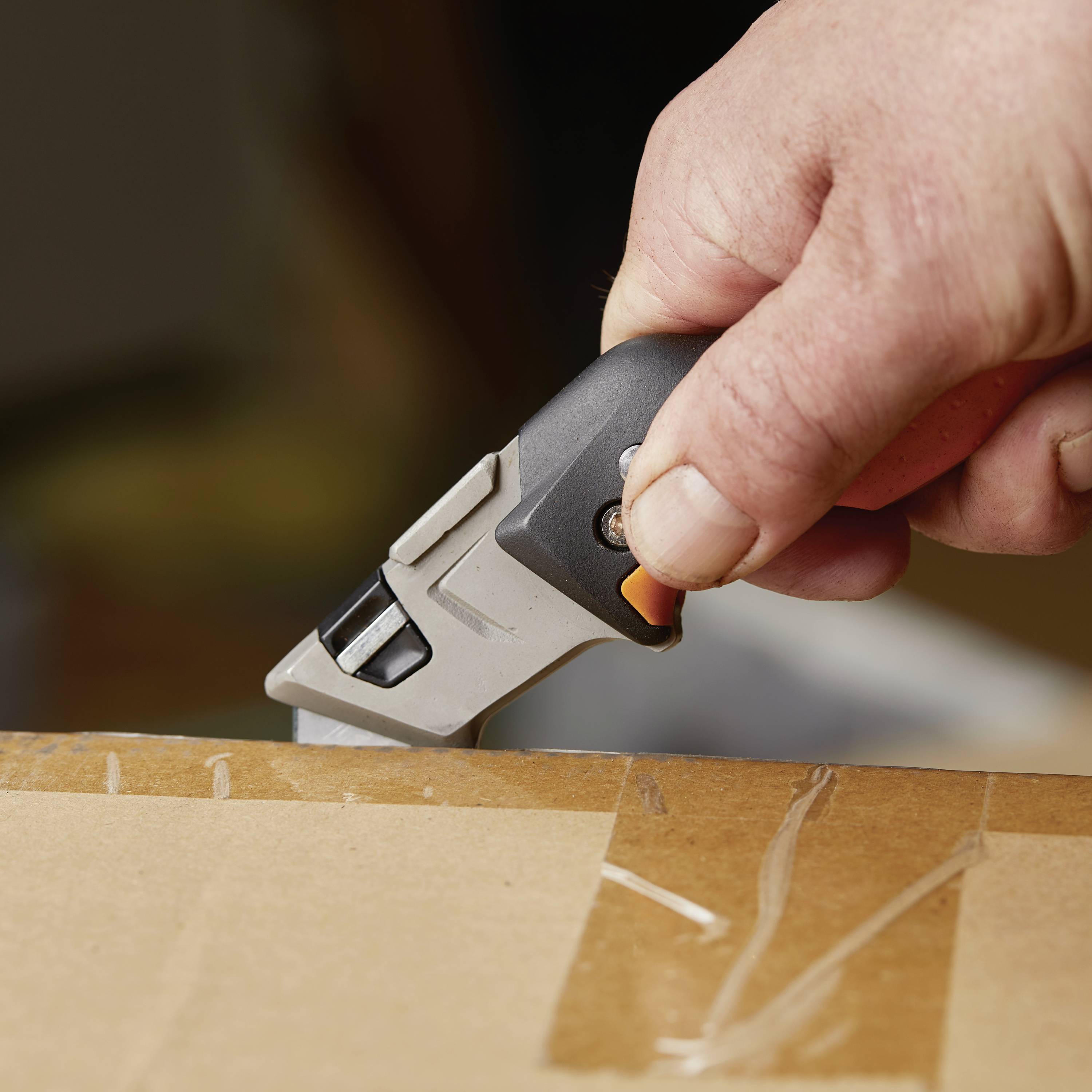 A hand cuts a cardboard box with a craft knife.