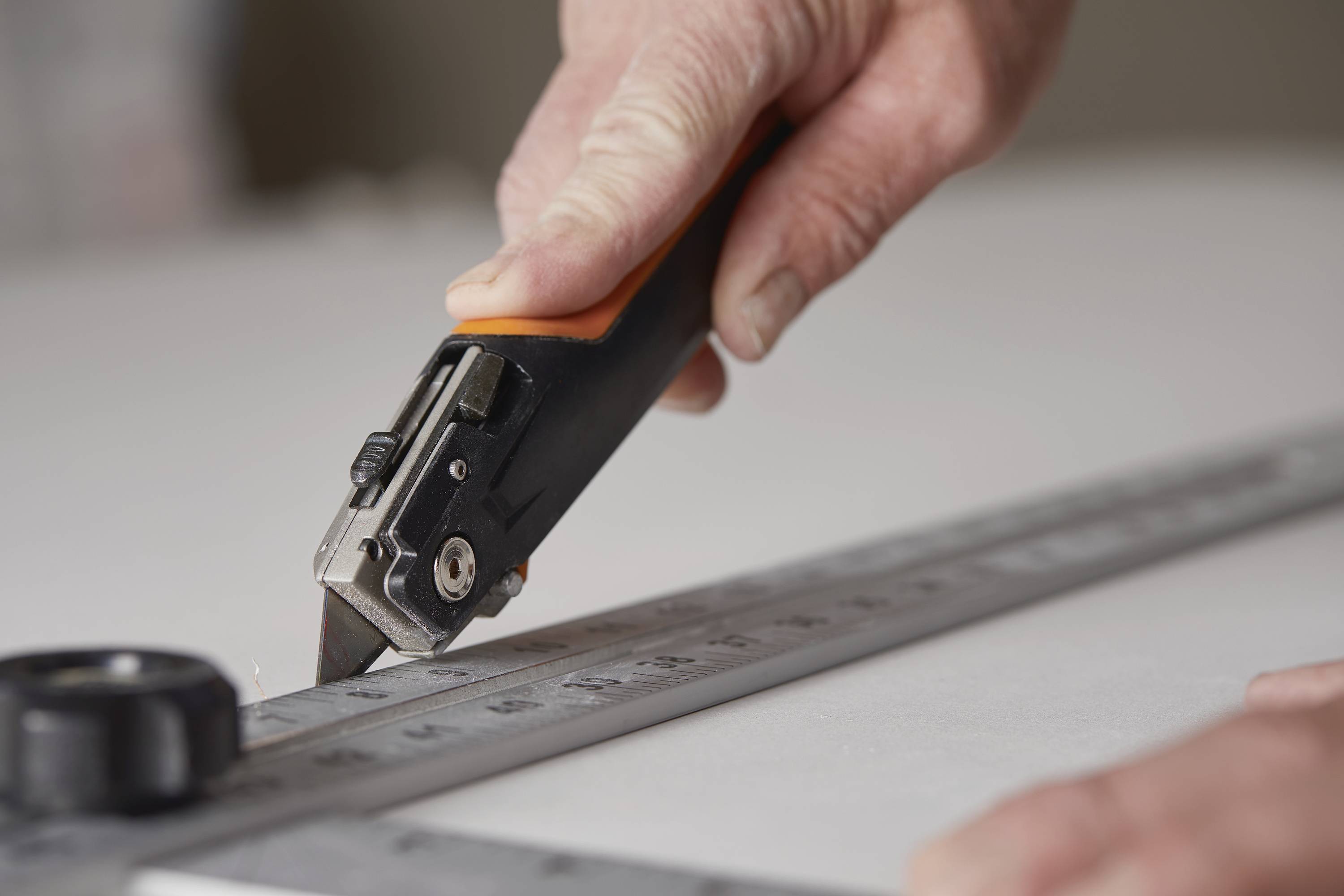 A hand is using a craft knife to cut precisely along a metal cutting ruler.