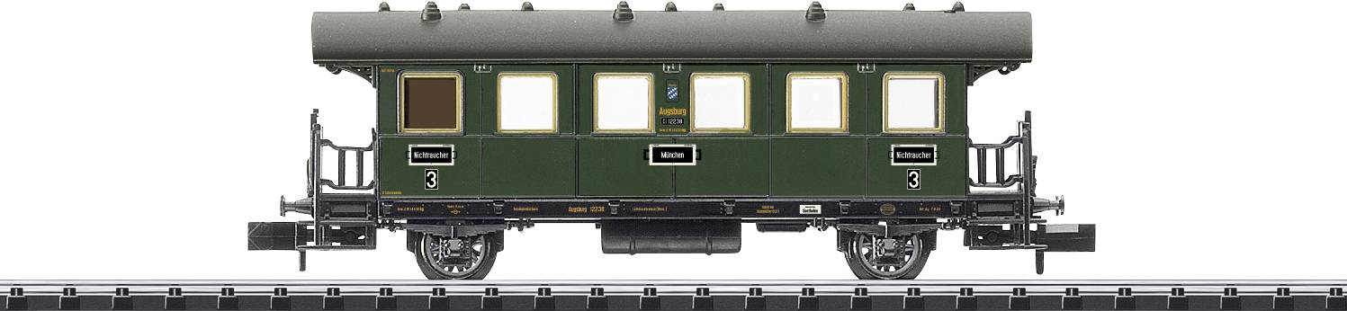 A green model railway carriage travels along a track. It is a historical passenger carriage with classic details.
