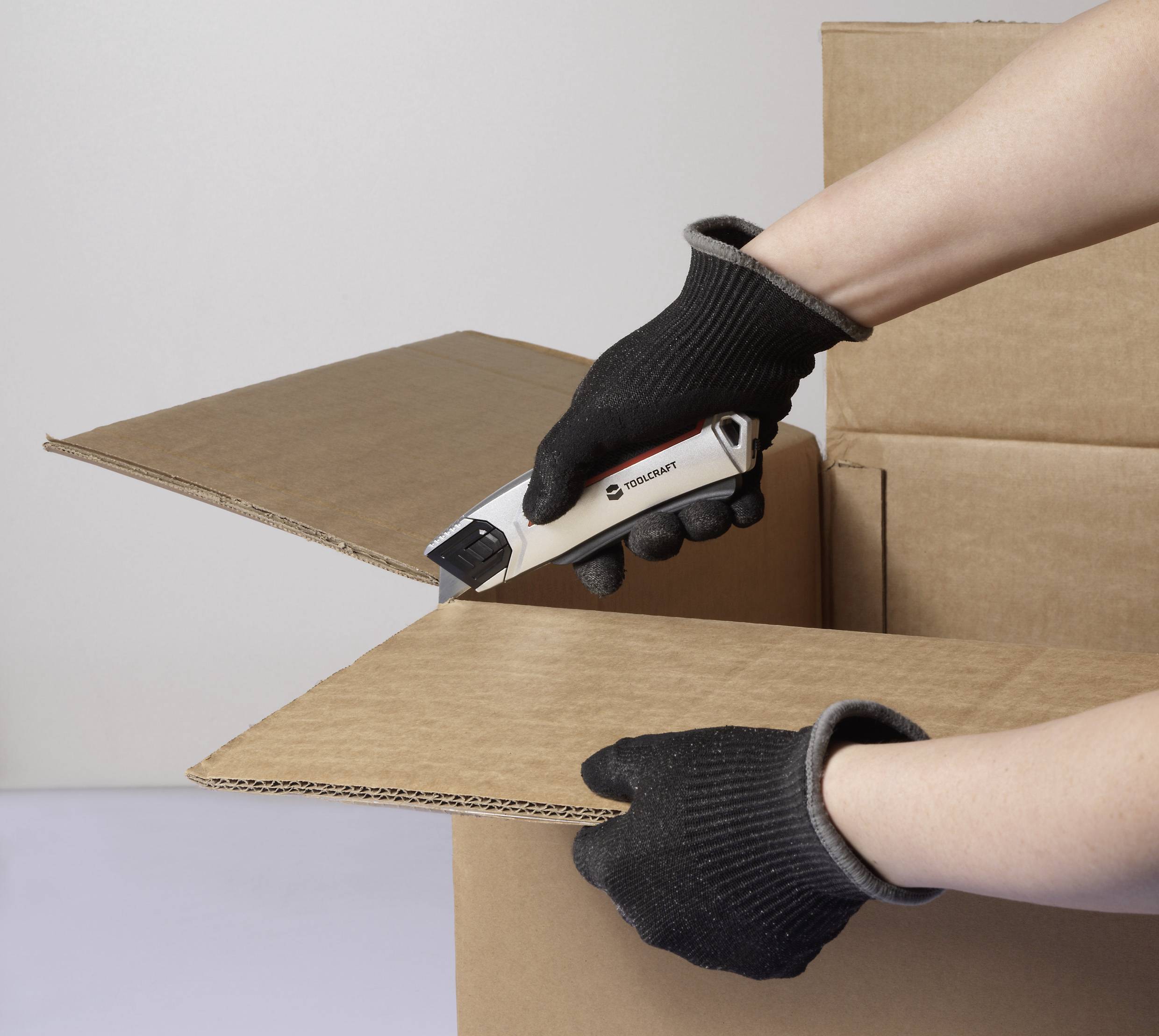 A person wearing gloves uses a safety box cutter to carefully open a cardboard box.