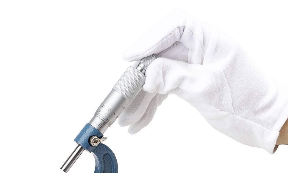 A hand wearing a white glove holds a blue micrometer, a precision measurement tool used to determine small distances or thicknesses.