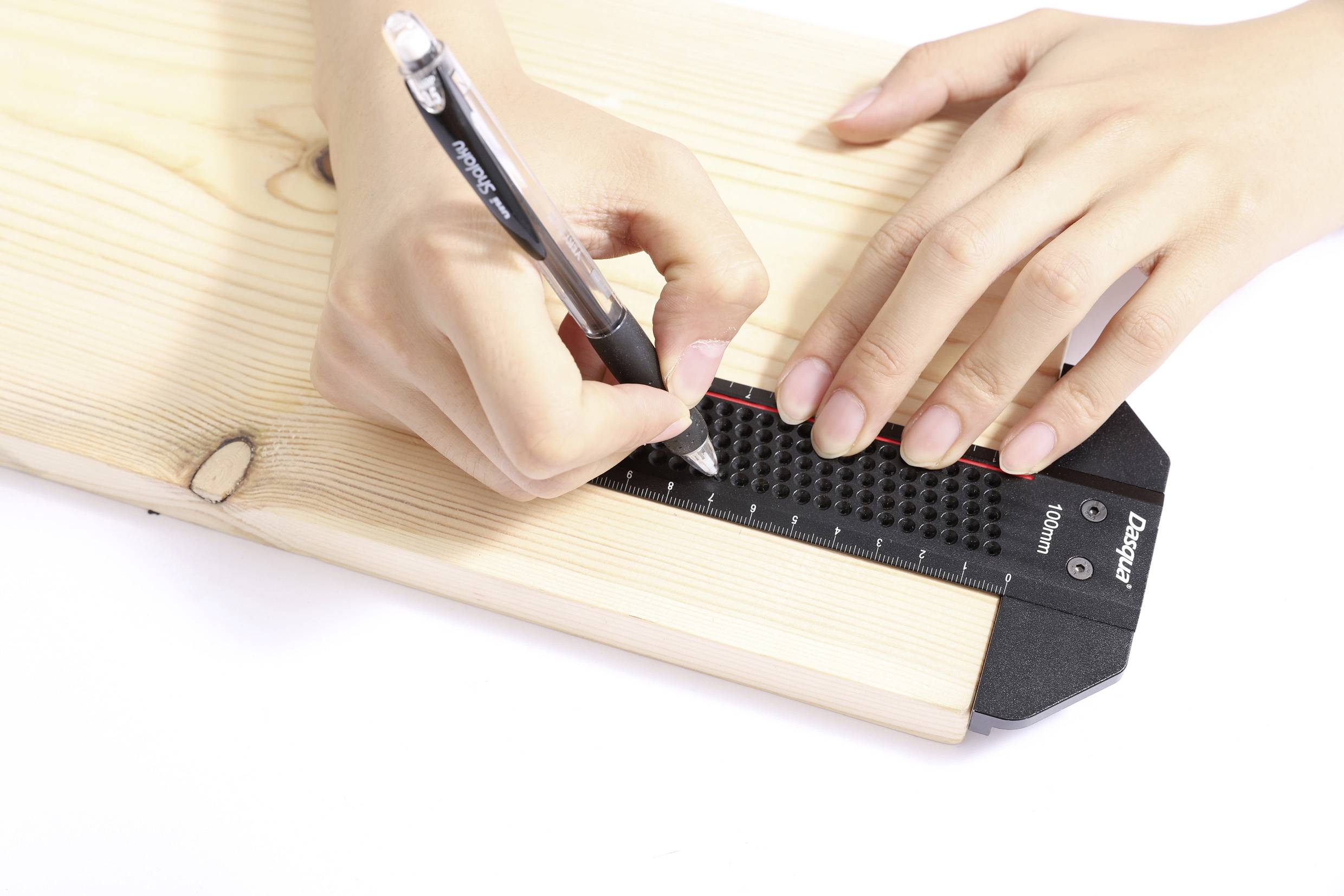 Two hands measure and mark a wooden plank using a black ruler and a pen, indicating an activity related to woodworking or construction.
