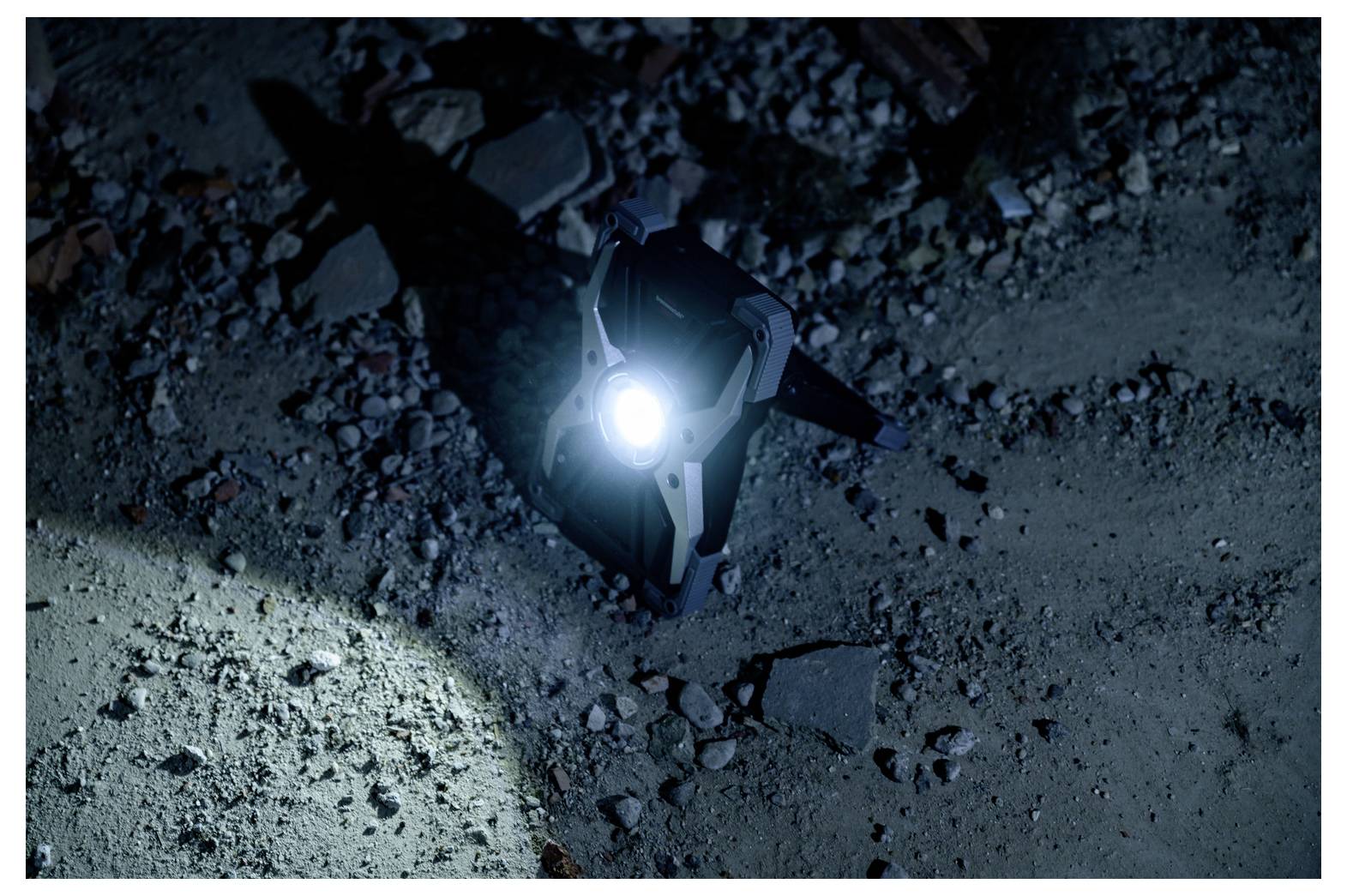 A small device with a bright light shines on rocky ground in darkness.