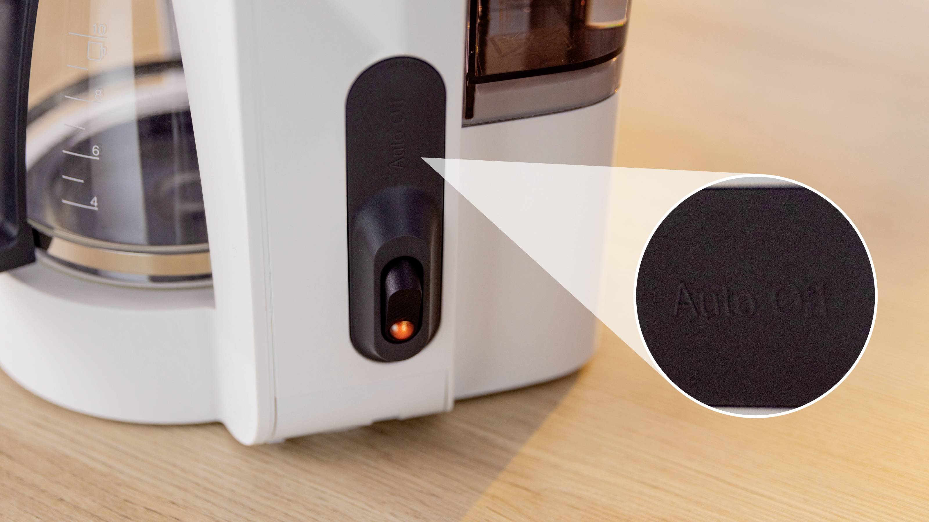 A white coffee maker with an illuminated power button labeled 'Auto Off' on a wooden surface.