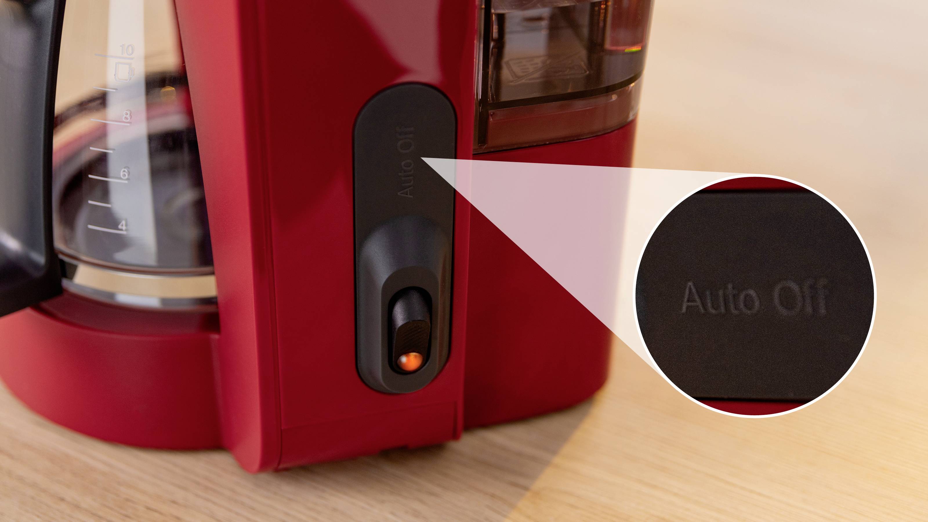 Close-up of a red coffee maker's switch labeled 'Auto Off', emphasizing the feature for automatic shut-off on a wooden countertop.