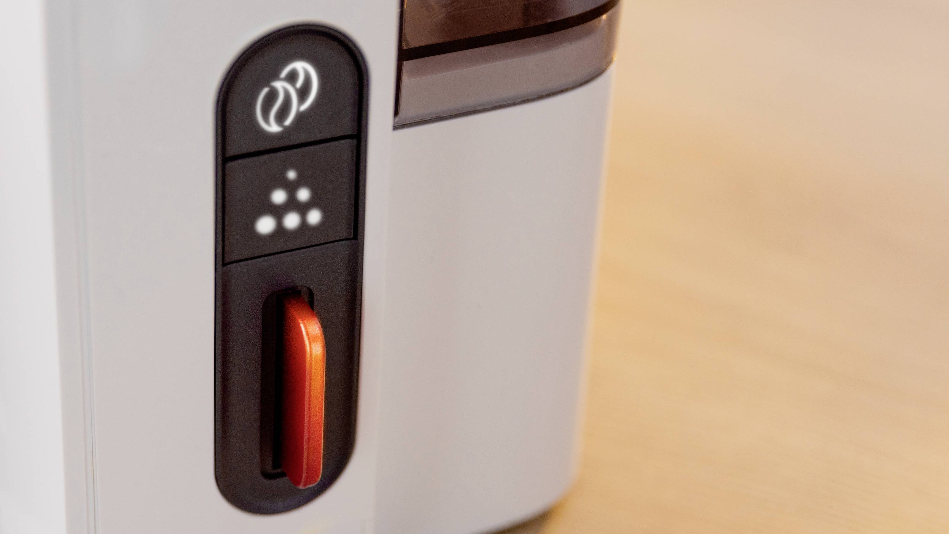 Close-up of a coffee machine's control panel, showing control symbols and an orange lever, set on a wooden counter.