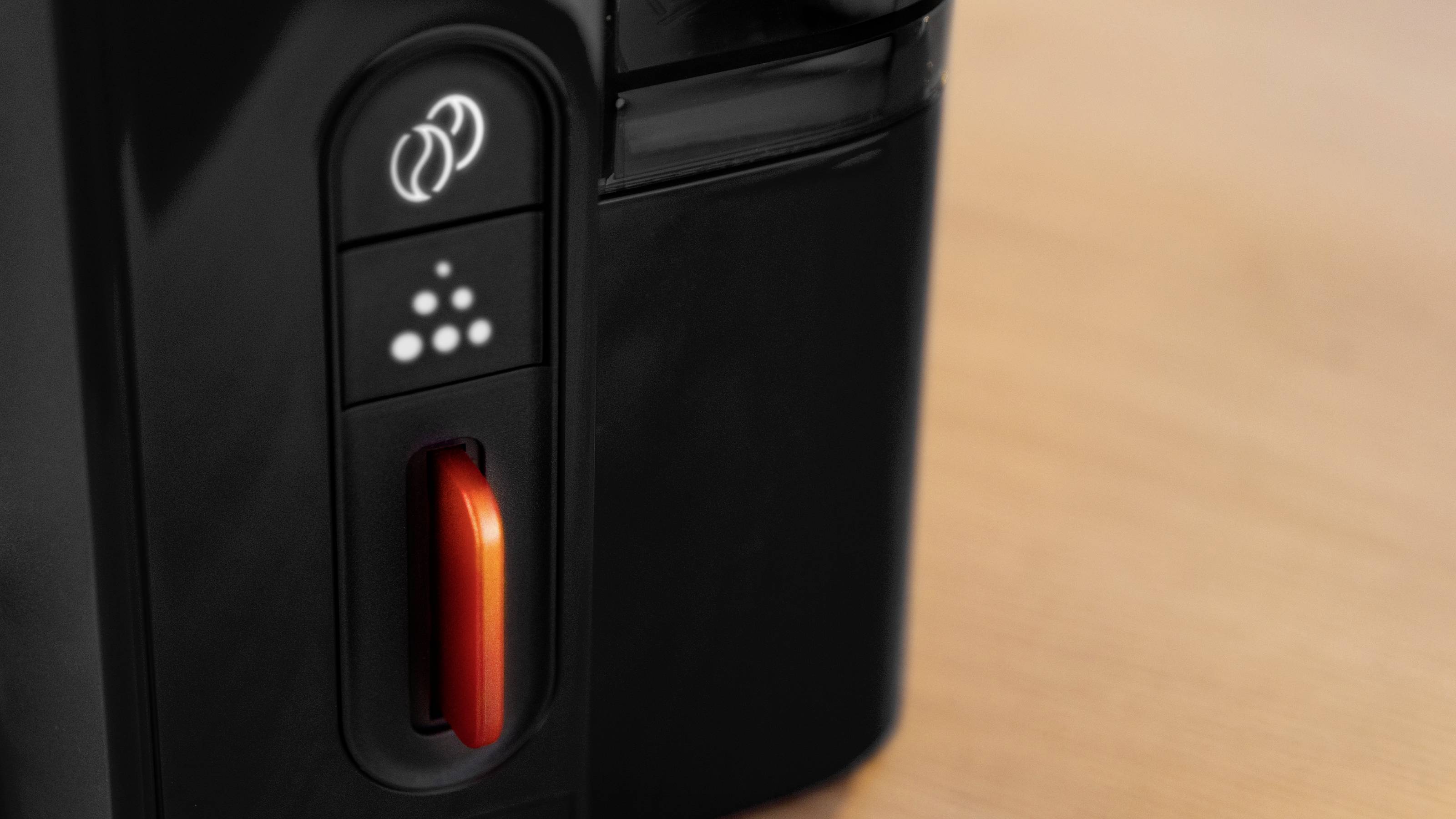 Close-up of a black and red coffee machine on a wooden surface, showing a power button and control panel.
