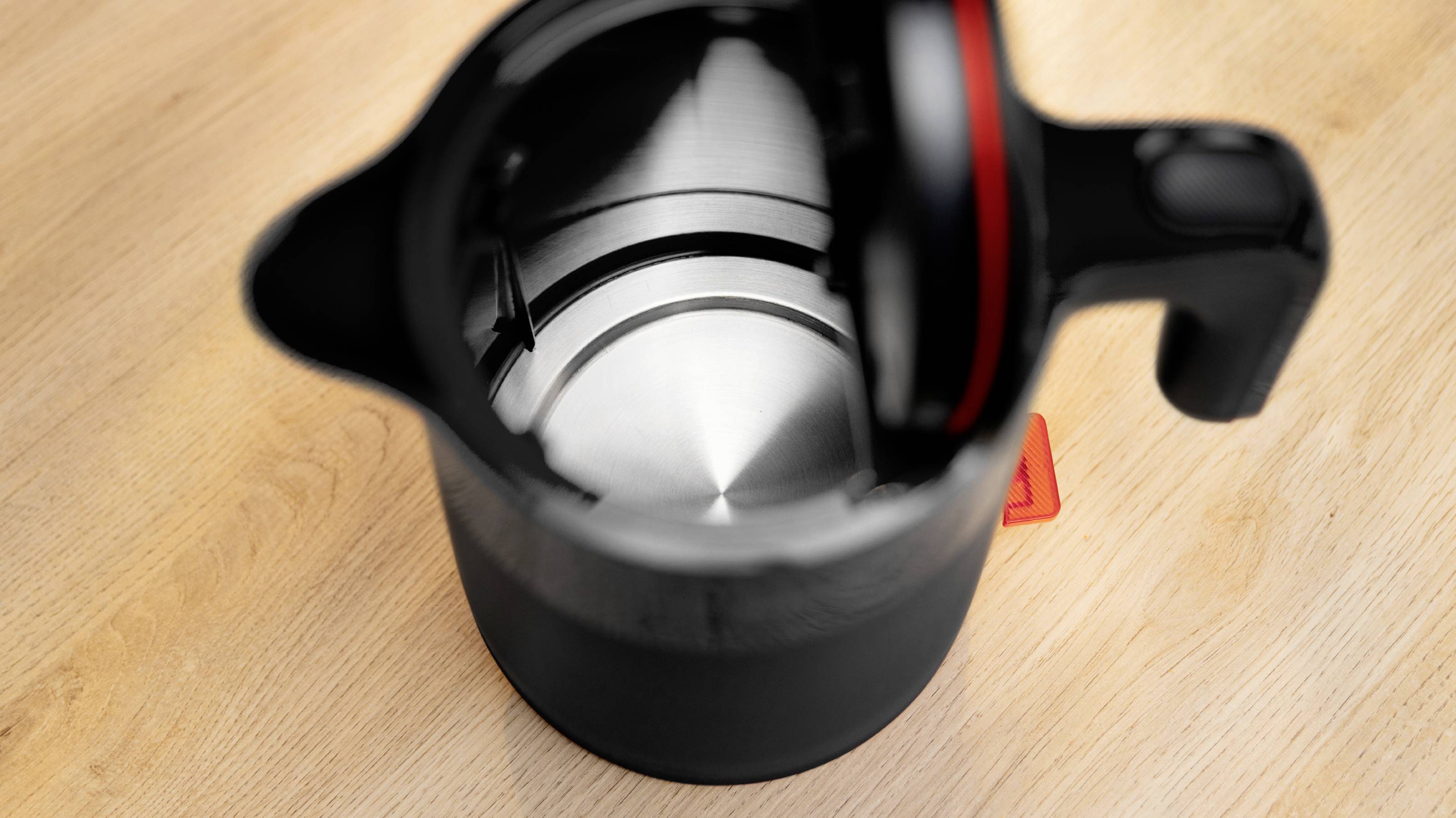 A black electric kettle with an open lid is placed on a wooden surface, showing its shiny metal interior.