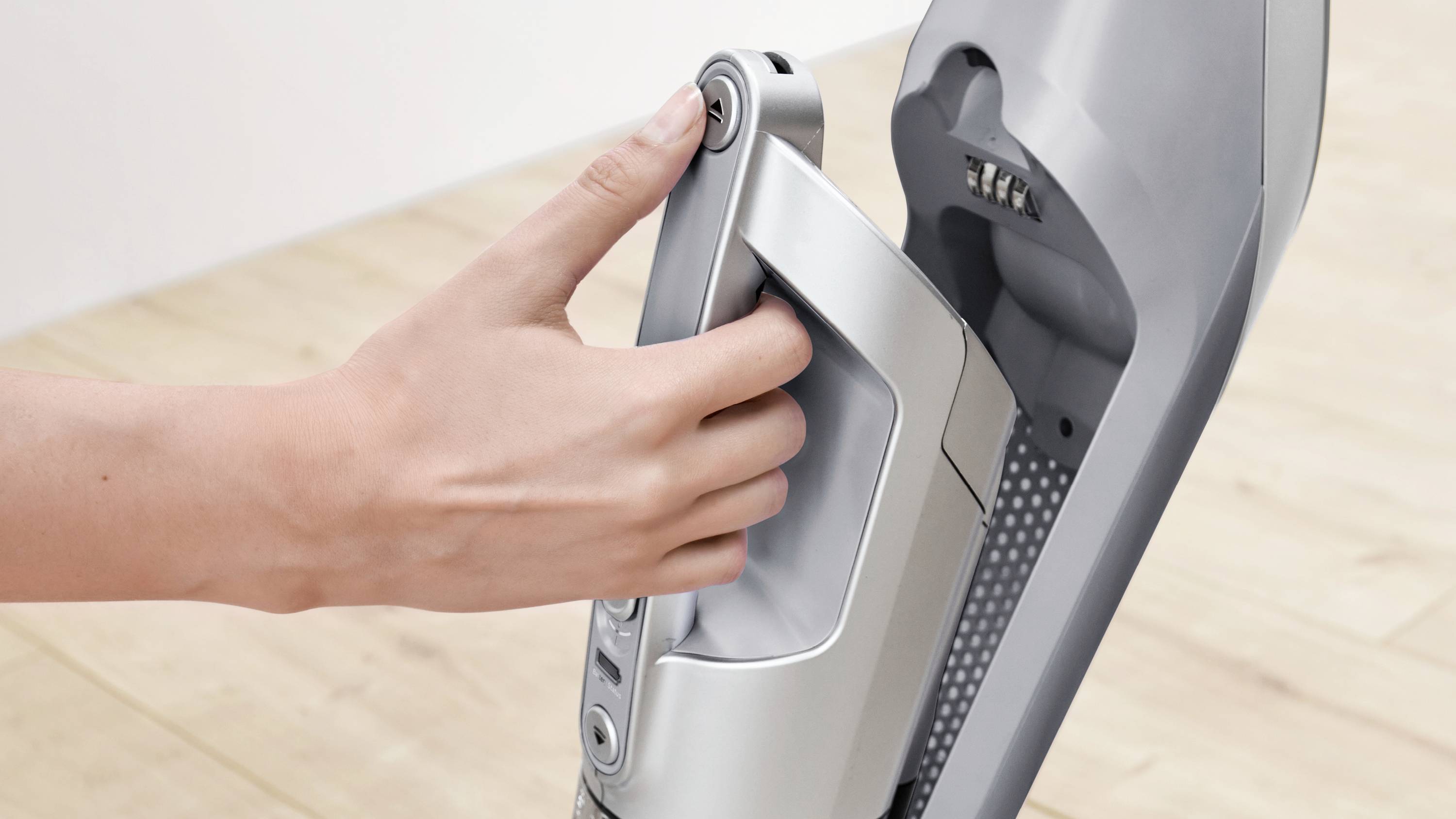 A person grips the handle of a gray, modern vacuum cleaner, suggesting easy removal of a detachable component on a wooden floor.