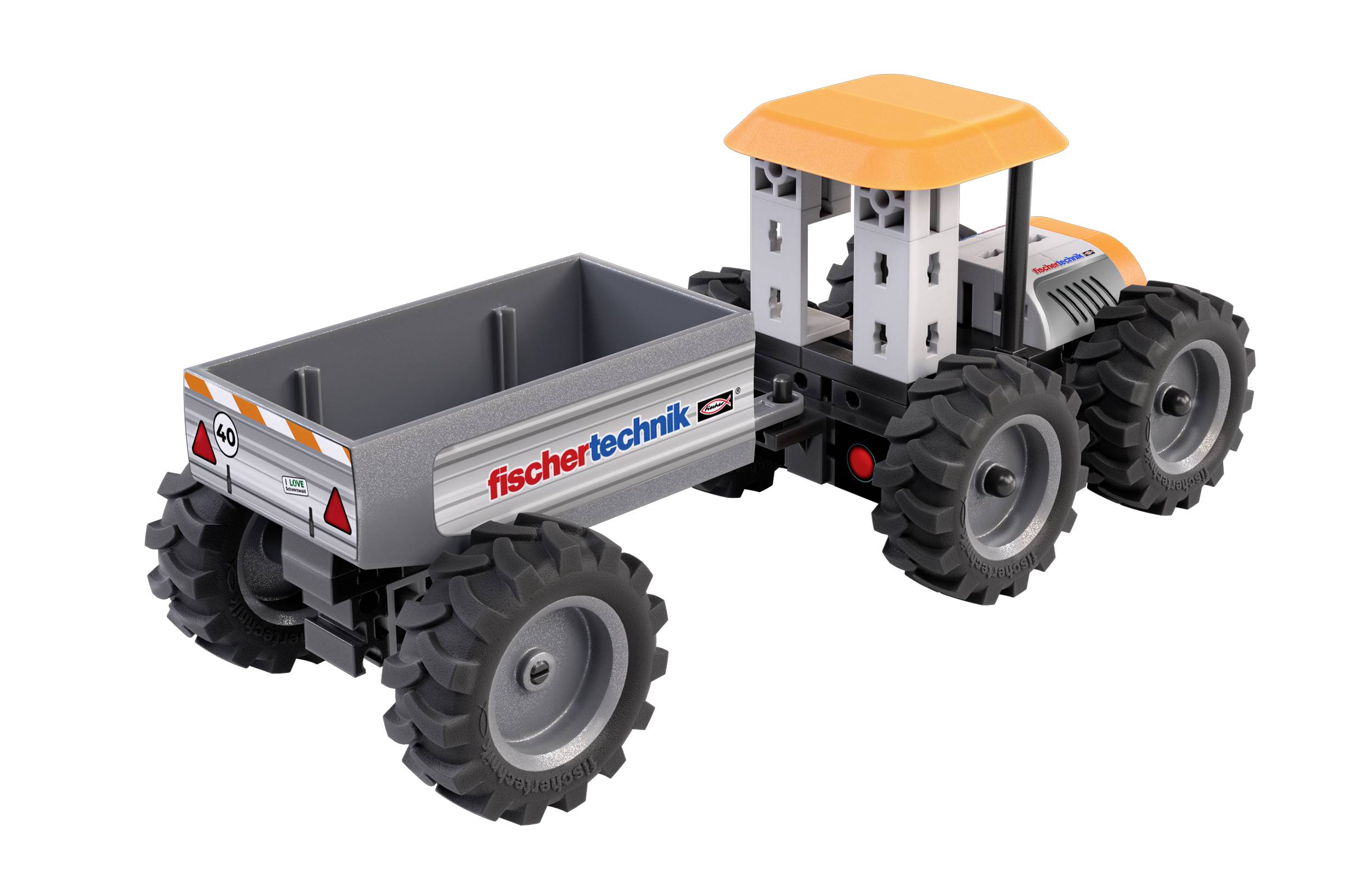 A toy tractor with a trailer, featuring 'fischertechnik' branding on the side, has large black wheels and a yellow roof.