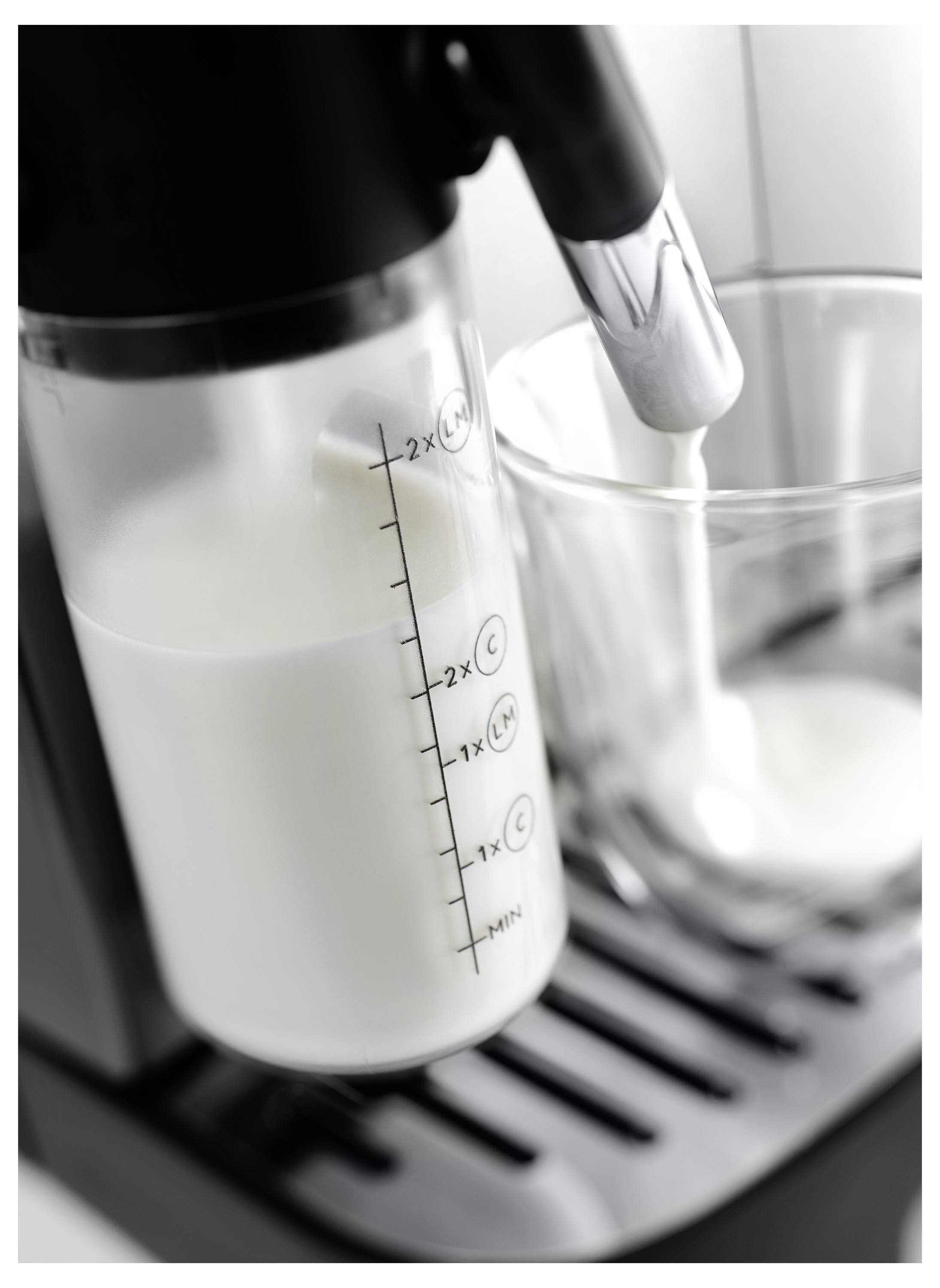 A milk frother is actively frothing milk into a clear glass placed on a tray, showing measurement markings on the frother container.