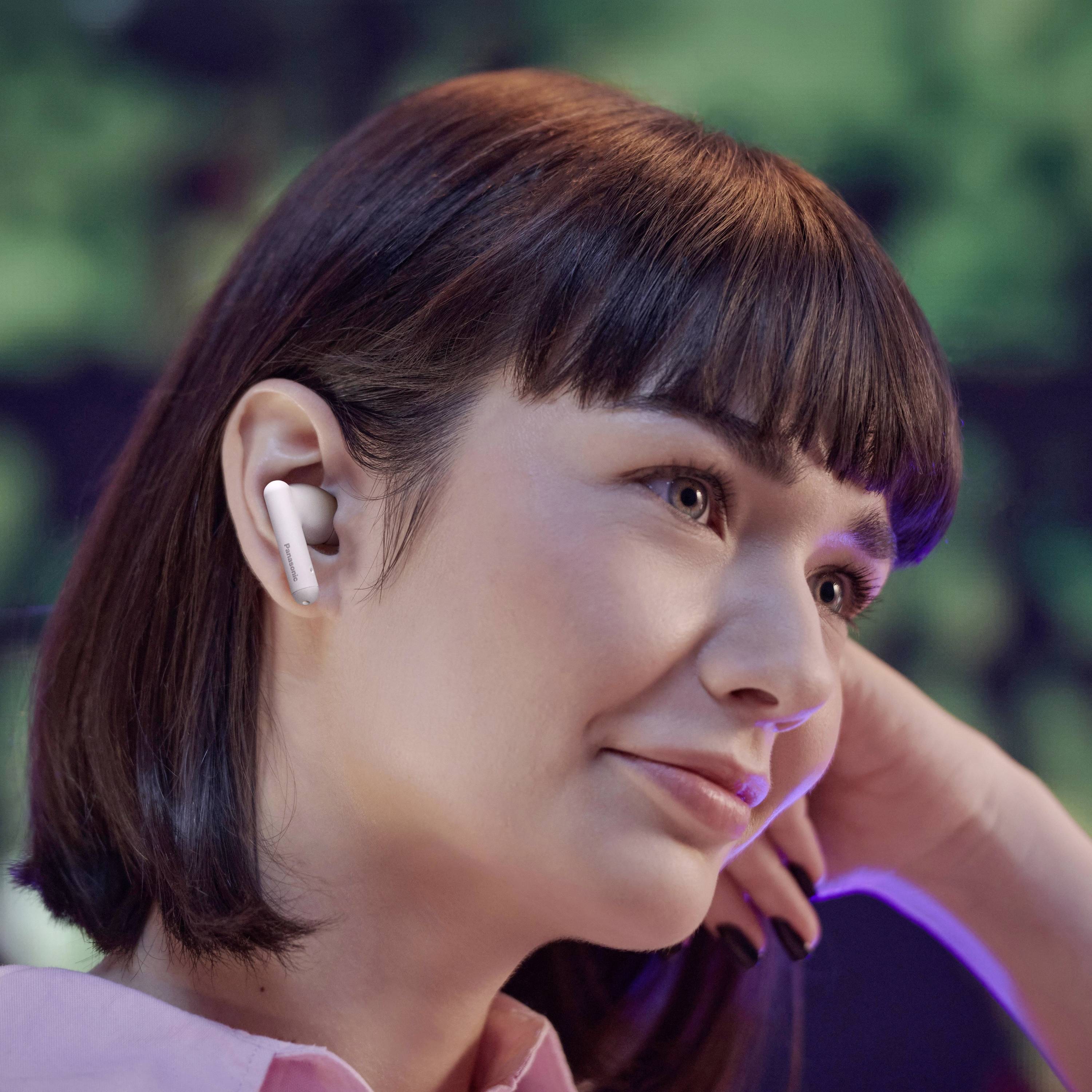 A person wearing wireless earbuds smiles, looking forward. The background is blurred, suggesting a relaxed or contemplative mood.