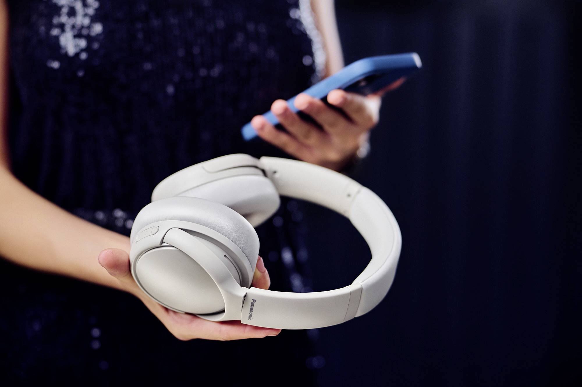 A person holding a smartphone and wireless headphones, focusing on technology and music accessibility.