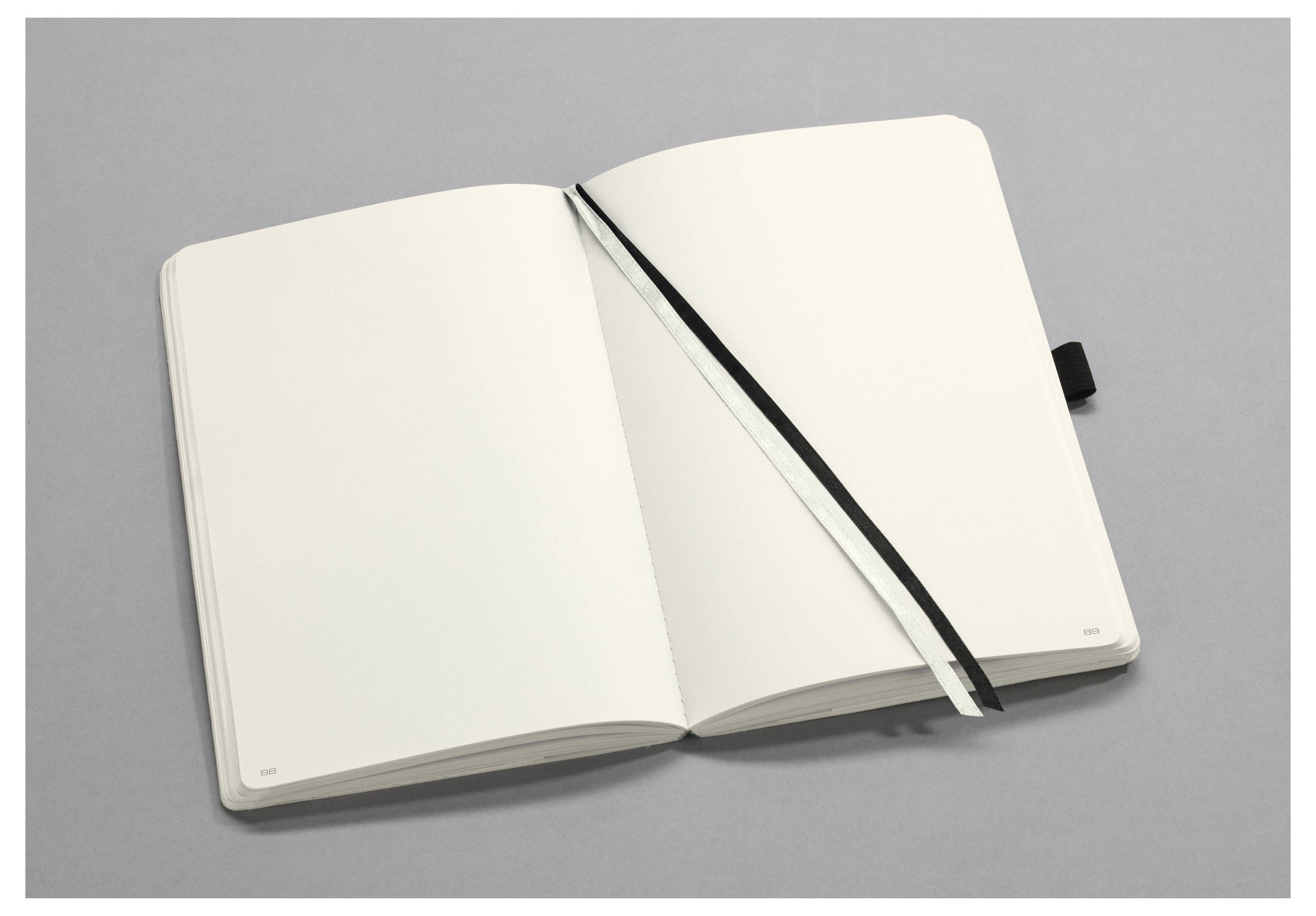 Open notebook with blank pages on a gray surface, featuring a black ribbon bookmark angled across the right page.