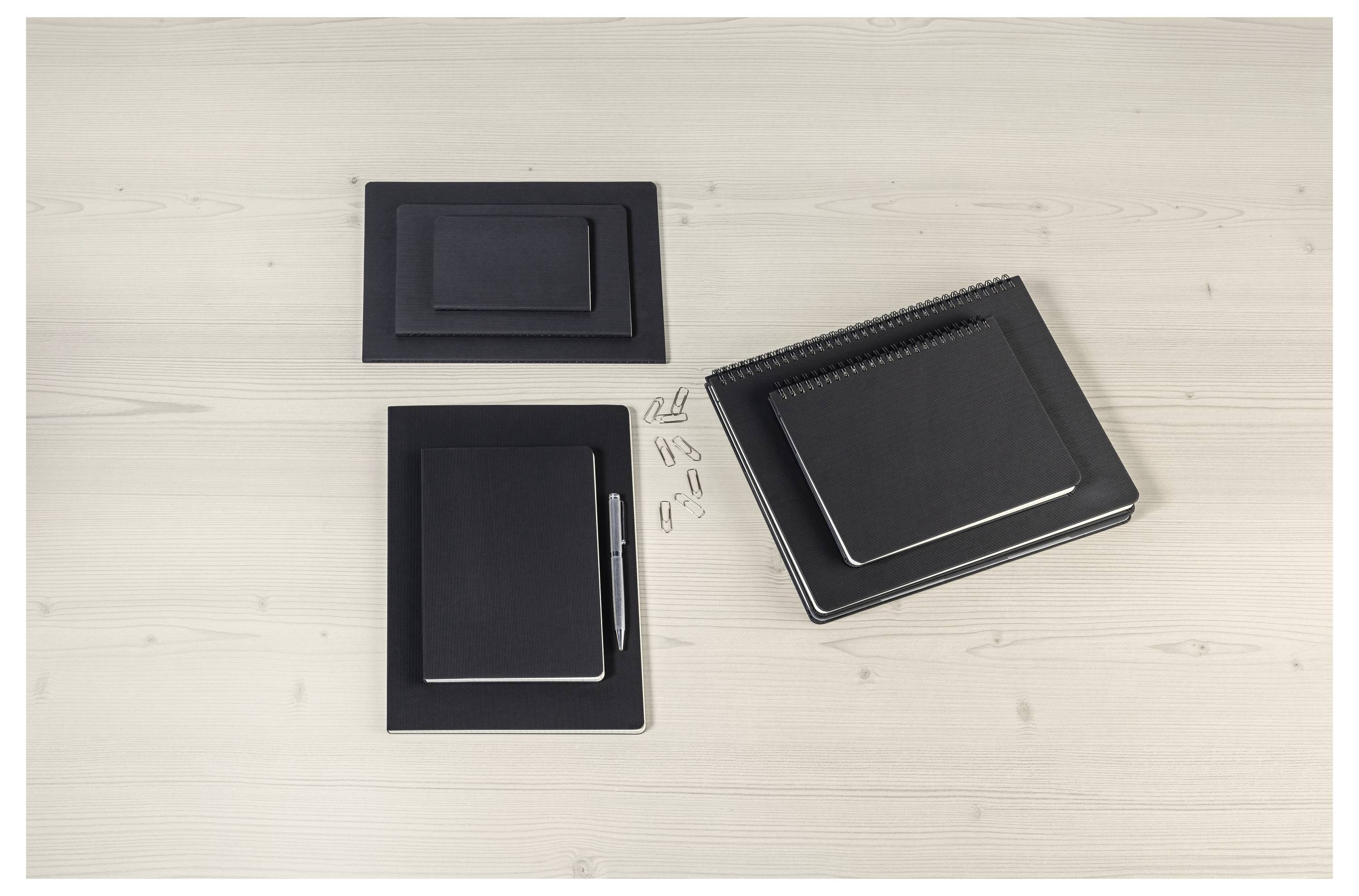 A set of black notebooks and notepads with a pen and paperclips arranged neatly on a light wooden surface.