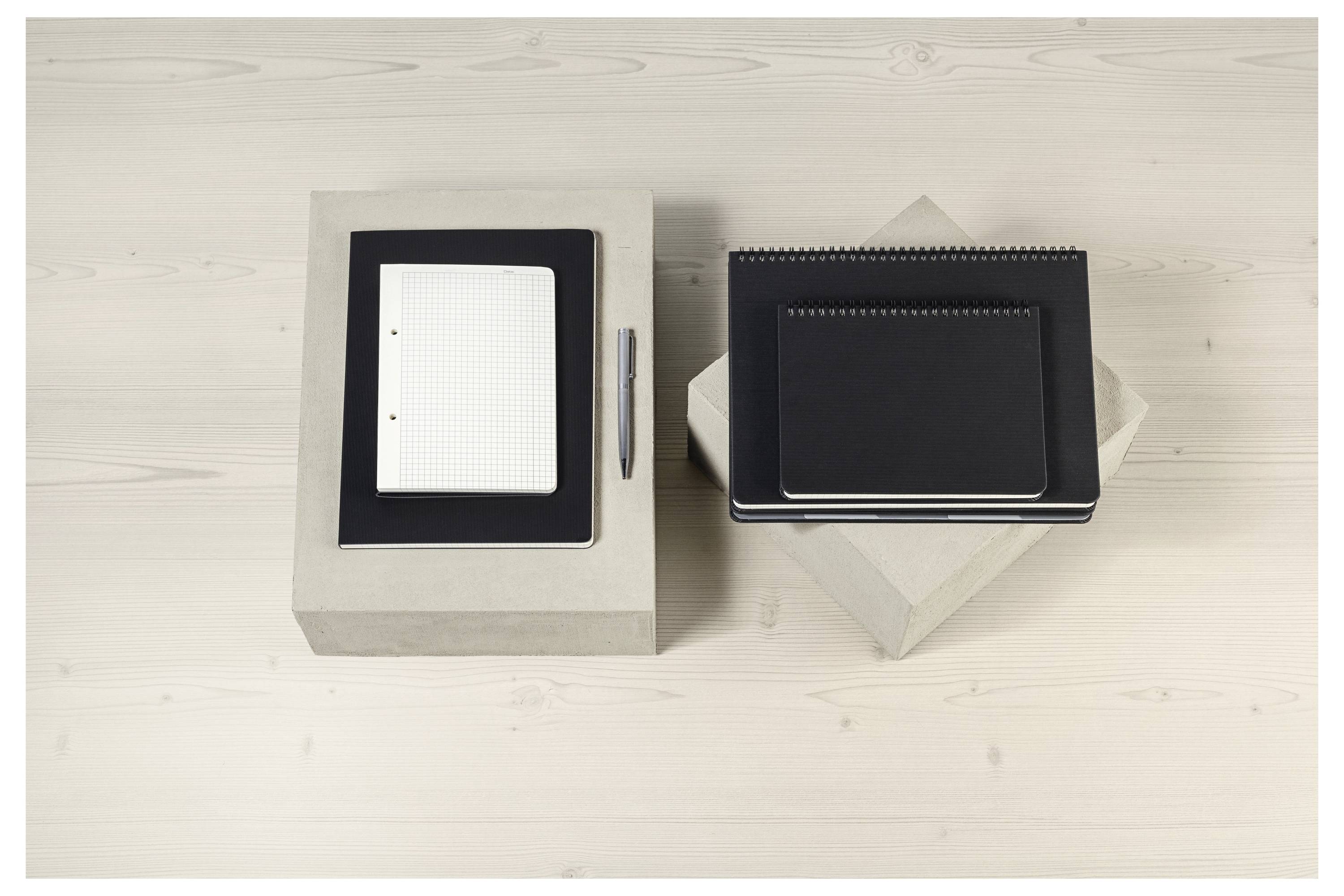 Two notebooks and a pen are placed on two square boxes on a wooden surface. The left notebook is white, and the right stack is black.