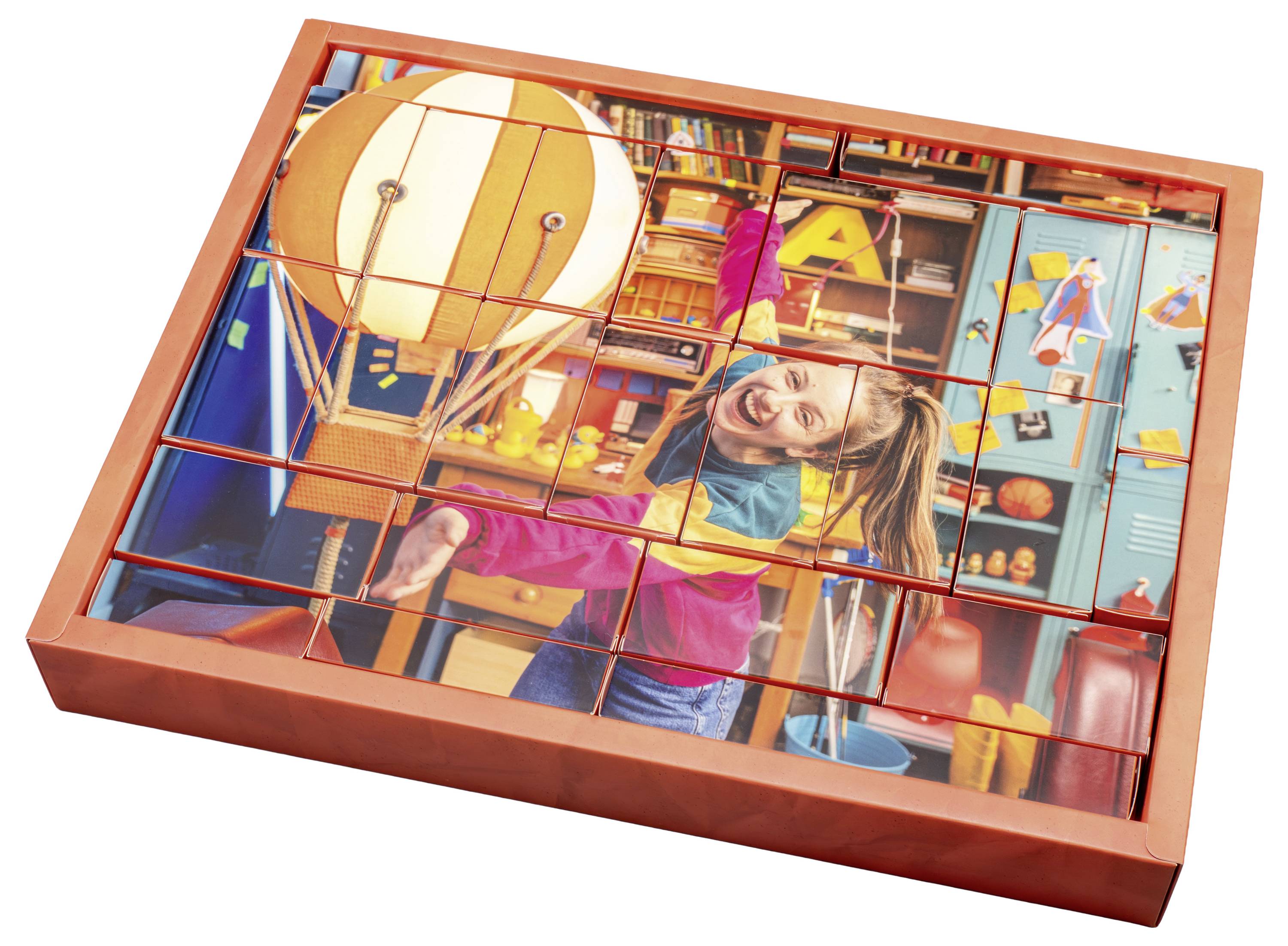 A girl with glasses and a colorful jacket smiles while posing by a classroom desk.