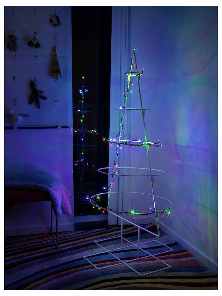 A wireframe Christmas tree with colorful LED lights stands in a dimly lit room with striped carpet, reflecting on nearby glass.