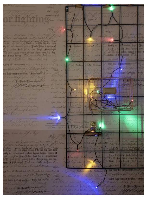 The image shows a wire grid against a script-covered backdrop. It is adorned with multicolored fairy lights in blue, green, yellow, and red.