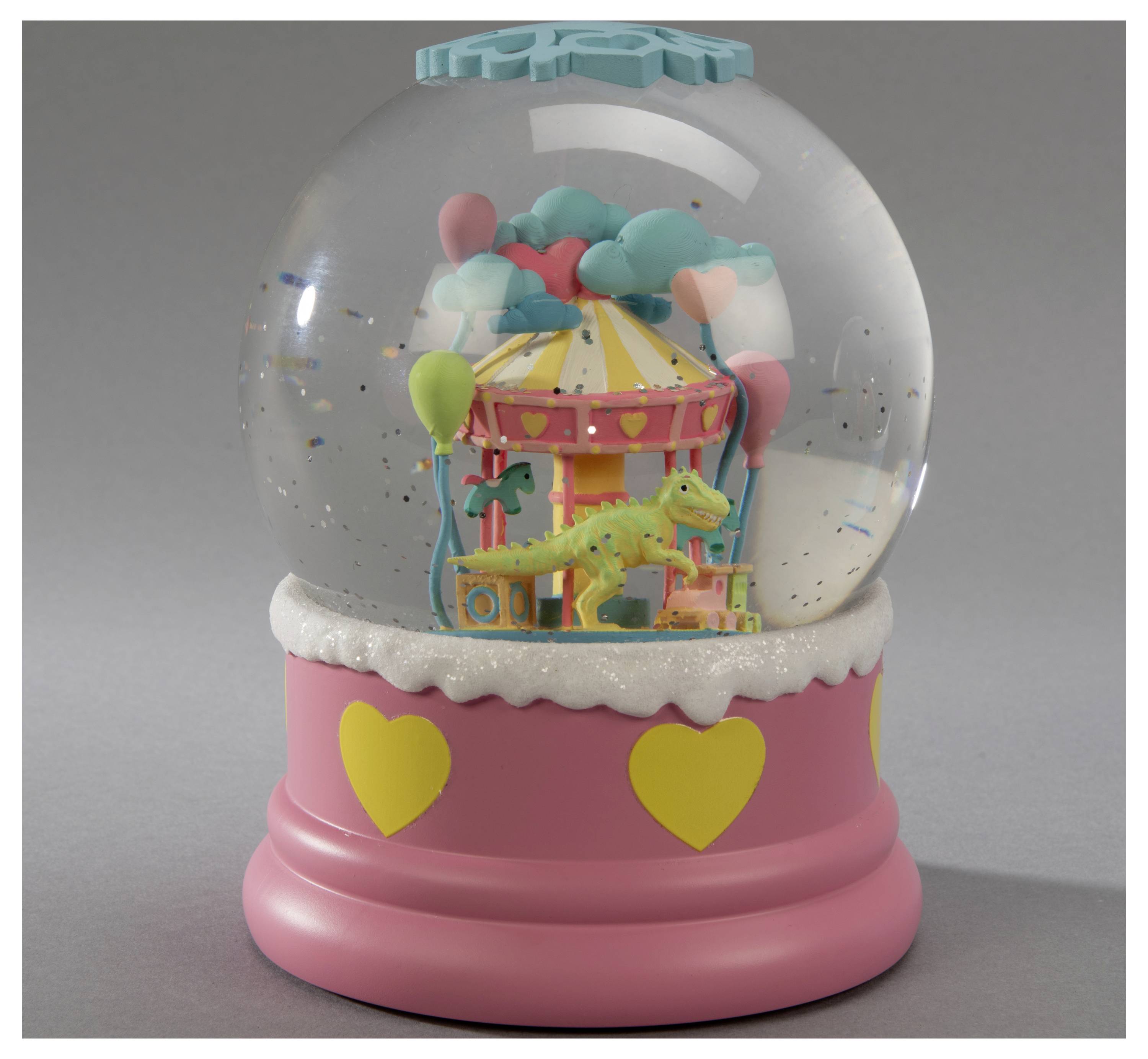 A colorful snow globe with a carousel inside, featuring a dinosaur and balloons, sits on a pink base with yellow hearts.