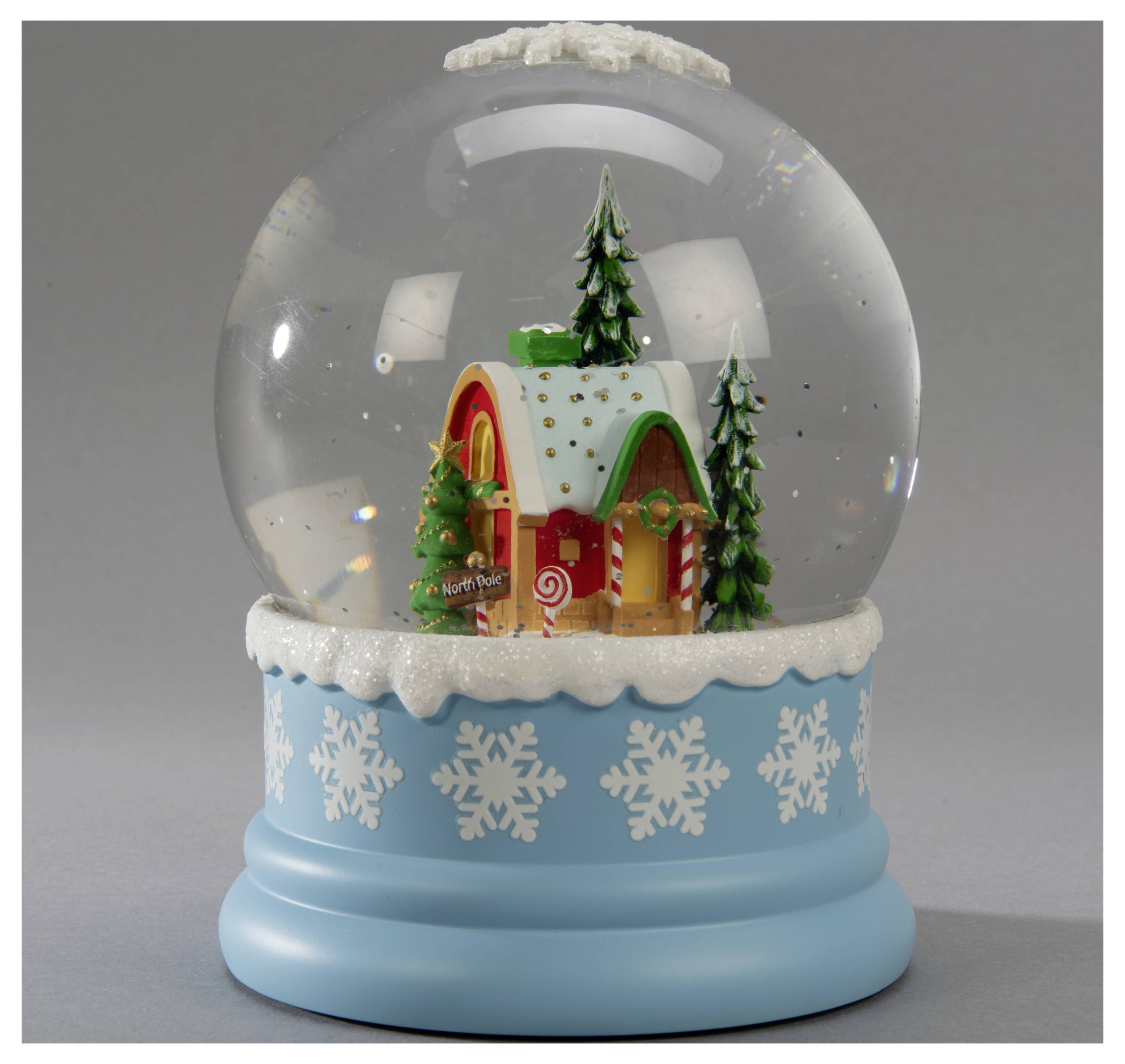 A snow globe featuring a festive house with snow-covered roof, surrounded by pine trees, on a blue base with white snowflake patterns.