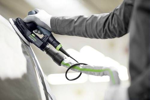 A person wearing gloves uses a polishing tool on a car's surface, focusing on the vehicle's glossy exterior.