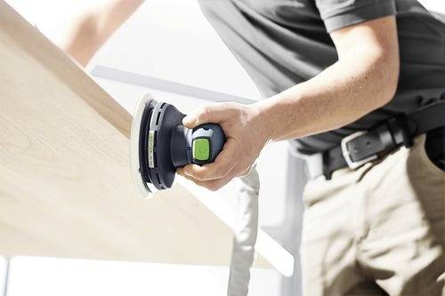 A person sands a wooden surface with a power sander, focusing on smooth finish work, in a bright indoor setting.
