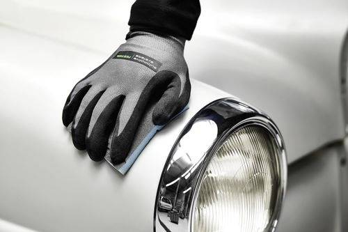 A gloved hand sanding a car's headlight on a white vehicle, focusing on restoration work. The glove has 'Green Corp' written on it.