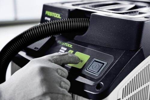 A person operates a Festool dust extractor, pressing the green 'ON' button. The device features a coiled hose and control interface.