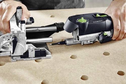 A person demonstrates using a woodworking tool on a perforated workbench. The tool appears to be a mortiser for joint creation.