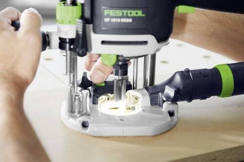 A person operates a Festool router, guiding it over a wooden surface. The tool is actively cutting, demonstrating woodworking in action.