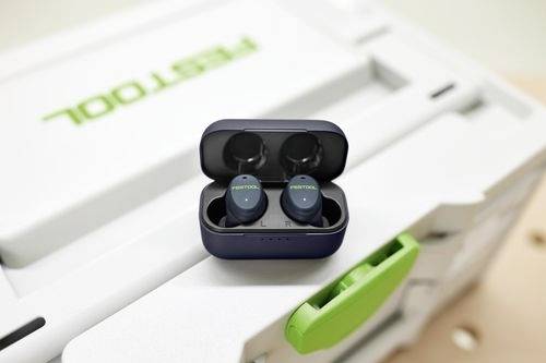 Earbuds with 'FESTOOL' branding inside a charging case, placed on a tool box, featuring a green latch.