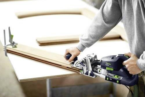 A person uses a joinery tool to connect wooden boards on a workbench.