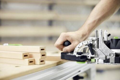 A person uses a biscuit joiner to cut slots into wooden boards, suggesting a woodworking or carpentry task in progress.