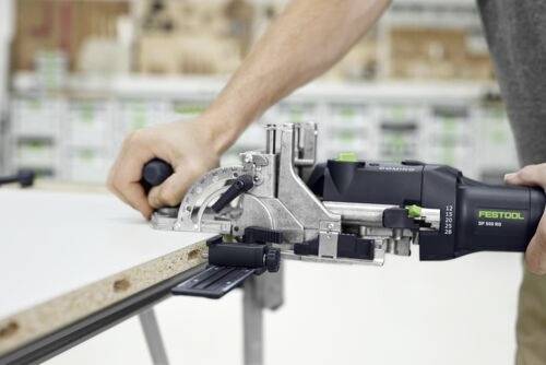 A person uses a Festool power tool to cut a piece of wood, showing precise measurement and control in a workshop setting.