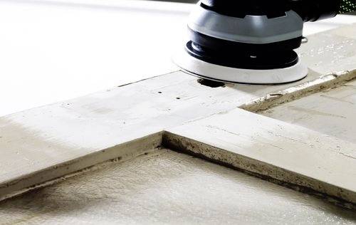 A close-up of a power sander smoothing a wooden surface, removing old paint.