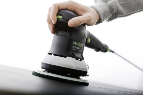 A person using an electric sander on a flat surface, focusing on the hand grip and sanding pad on the tool.