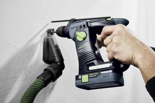 A person uses a cordless power drill with a dust extraction attachment on a white wall, demonstrating a dust-free drilling solution.